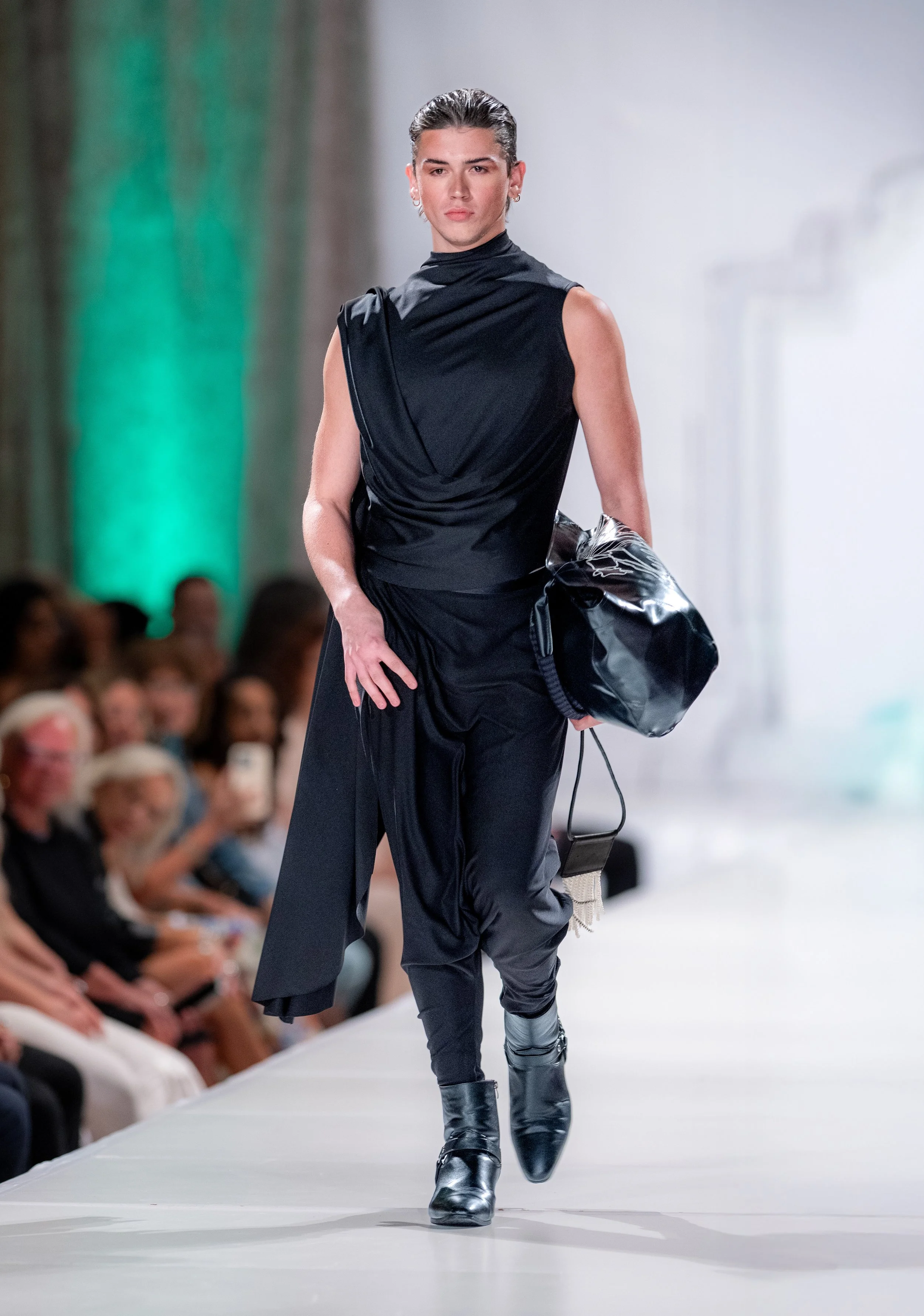 Black sleeveless mock-neck top with draped front and scarf-effect back, paired with black drop crotch trousers featuring two pockets. Black vinyl tote bag with interior pocket and hand-guided machine embroidery featuring original artwork.