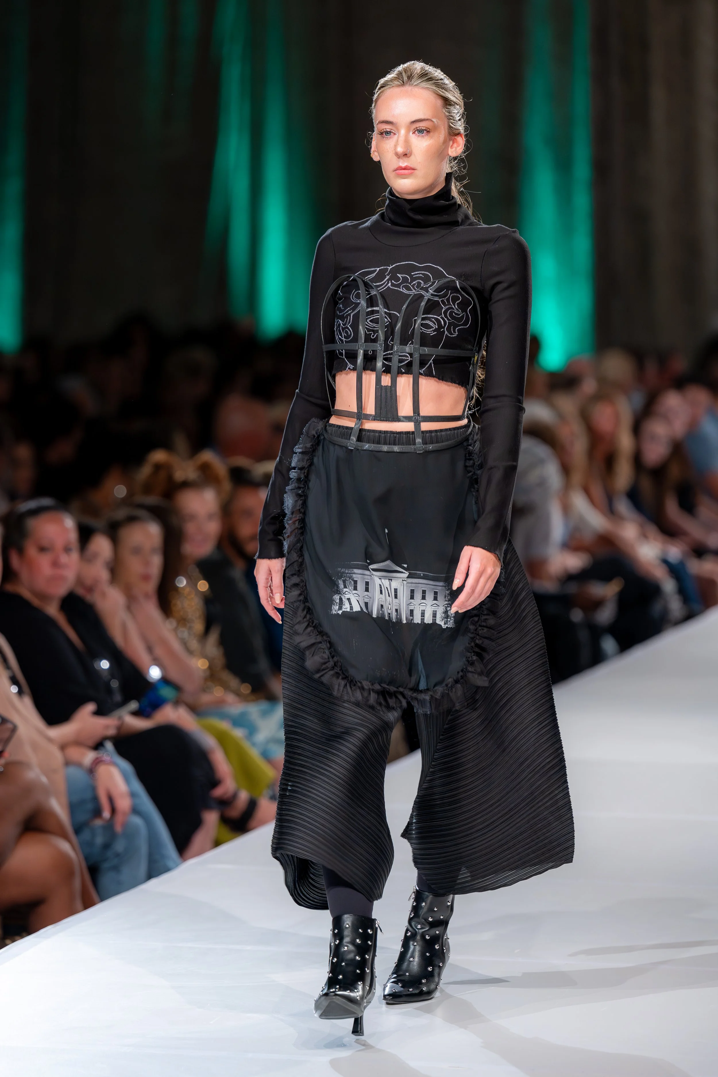 Pleated polyester, black pants with pockets, Deconstructed corset apron with sublimation print of the White House, with "crying boy" black ponte knit turtleneck crop top. 

Kansas City Fashion Week F/W 2025