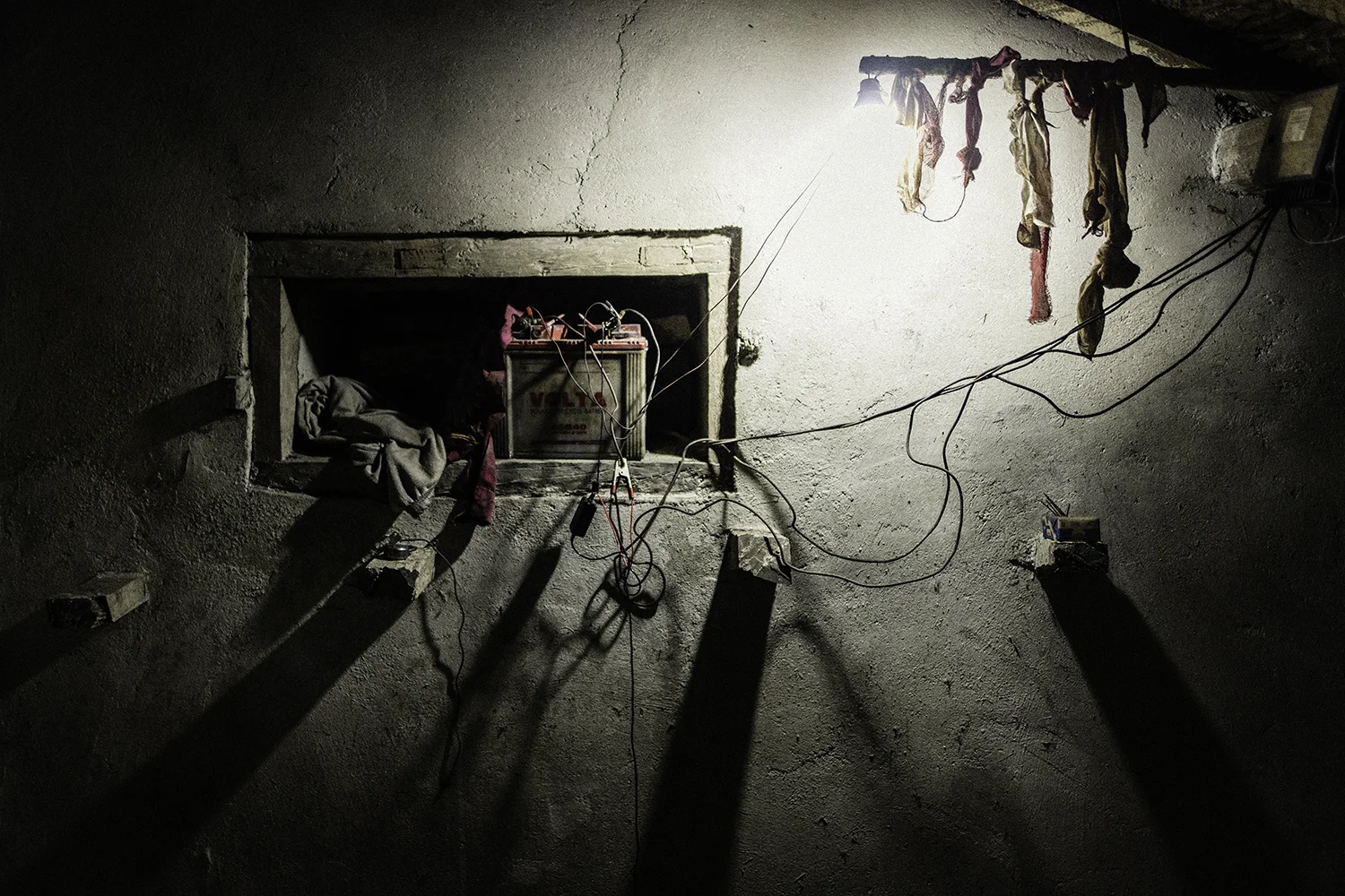 A car battery provides light for one bulb and a group of phone chargers. 