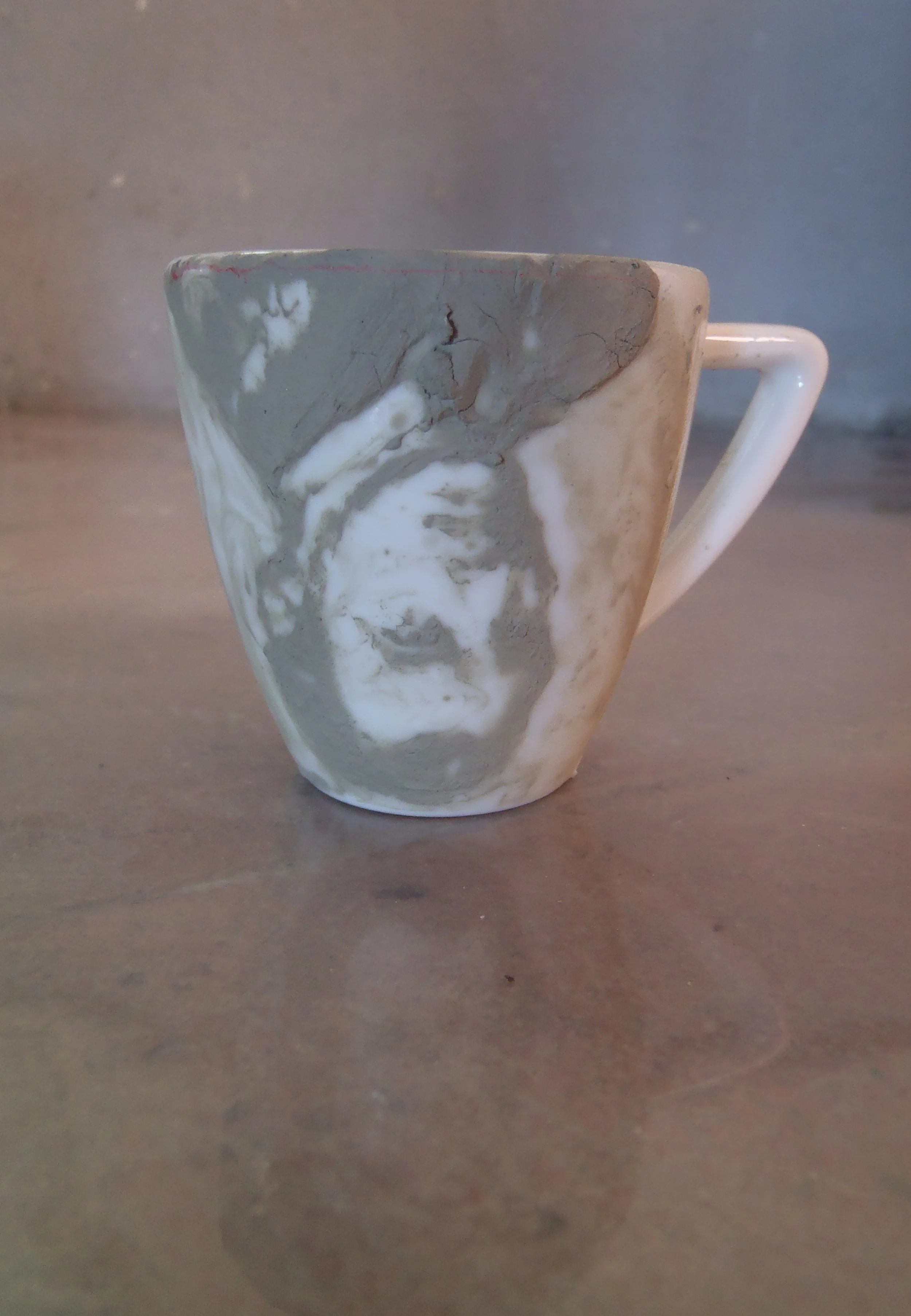   Remains,  2012  Clay on porcelain cup, washed    In  Remains,  I question what contents we leave behind postmortem. What are the lasting impressions, material and immaterial, that we leave behind? What constructs are washed away? 