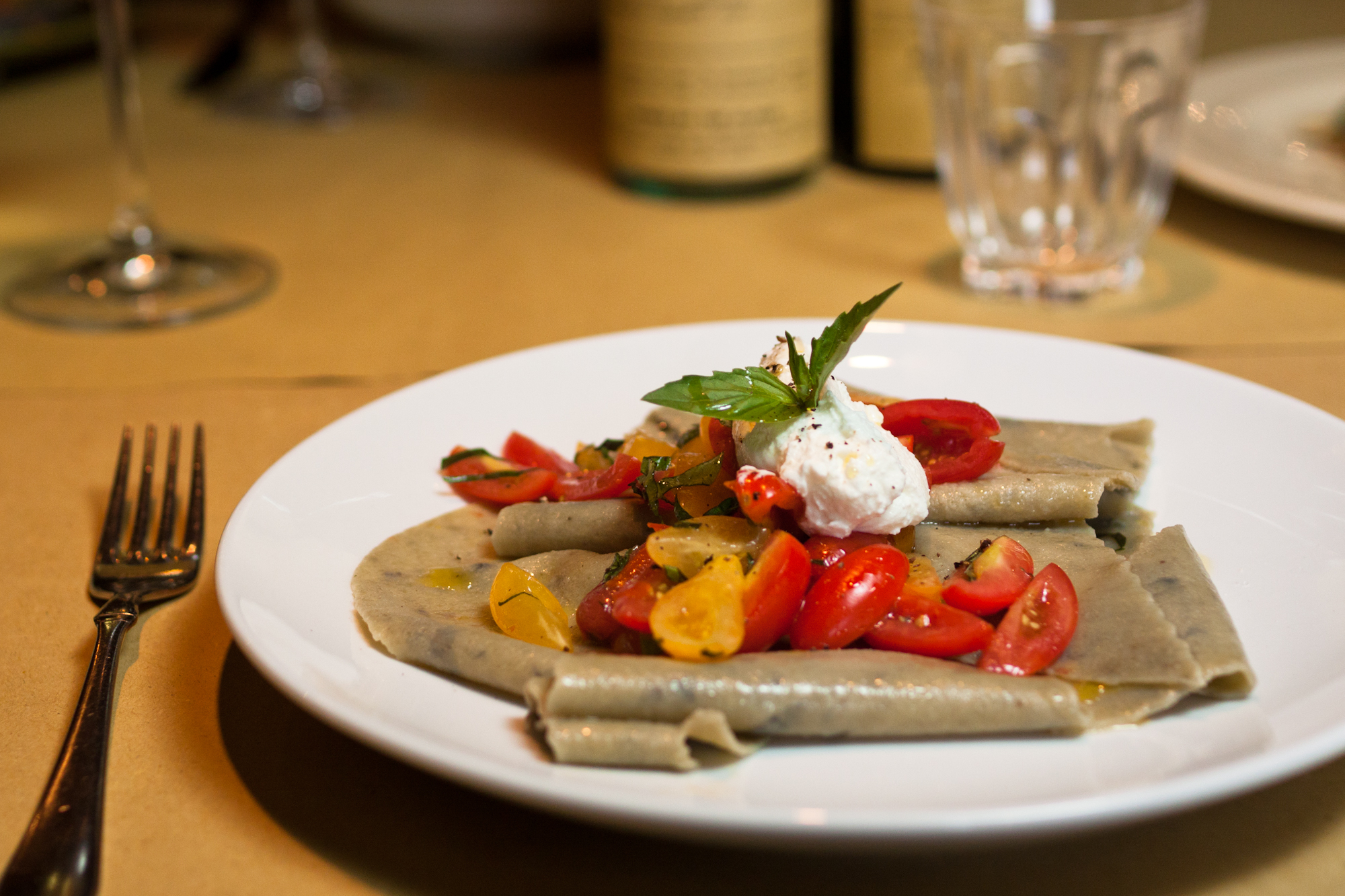 Basil maltagliati fresh pasta with cherry tomatoes and ricotta on a nice table