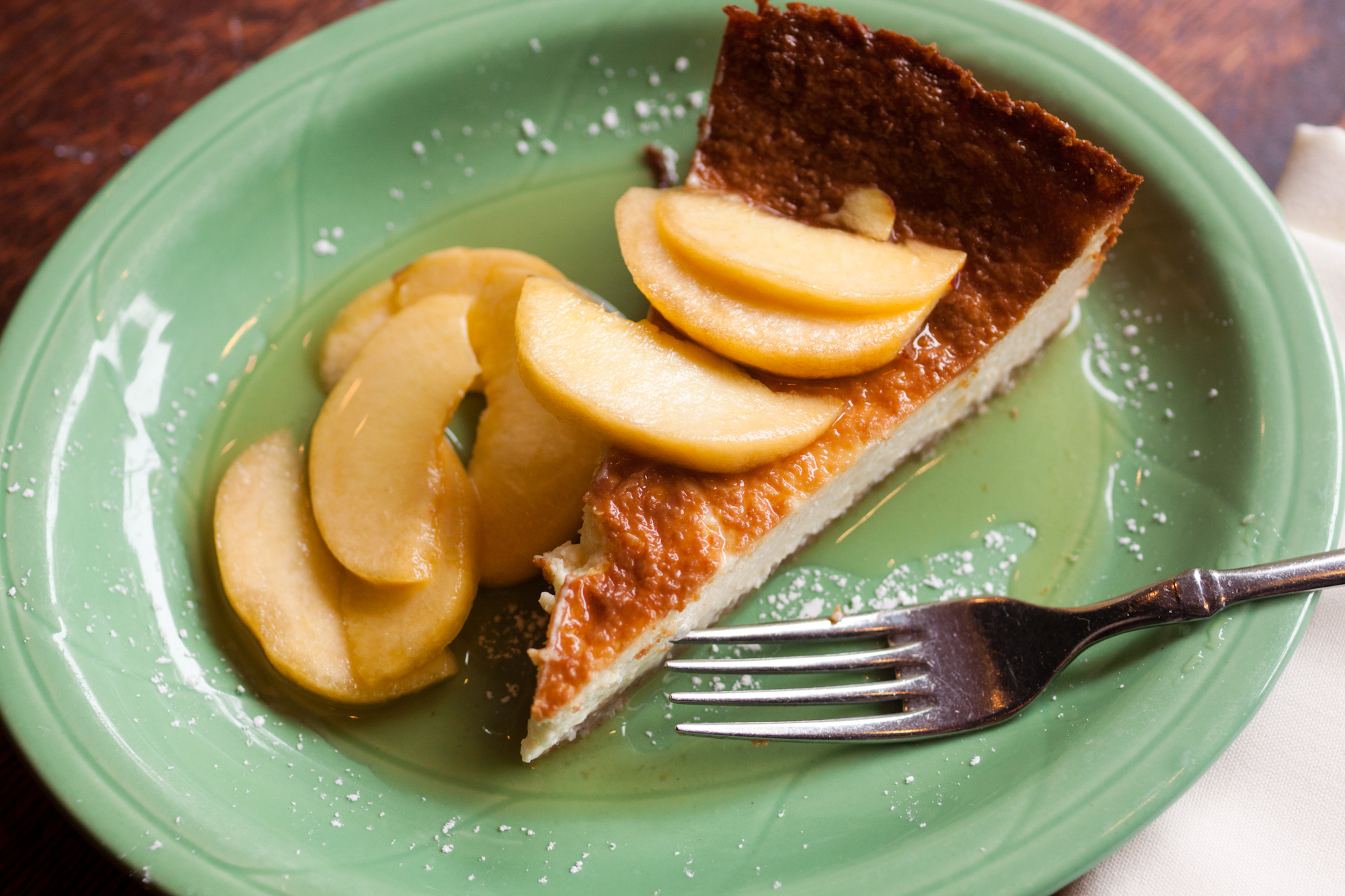 A slice of ricotta and caprino cheese cake with sliced peaches in honey on a green plate