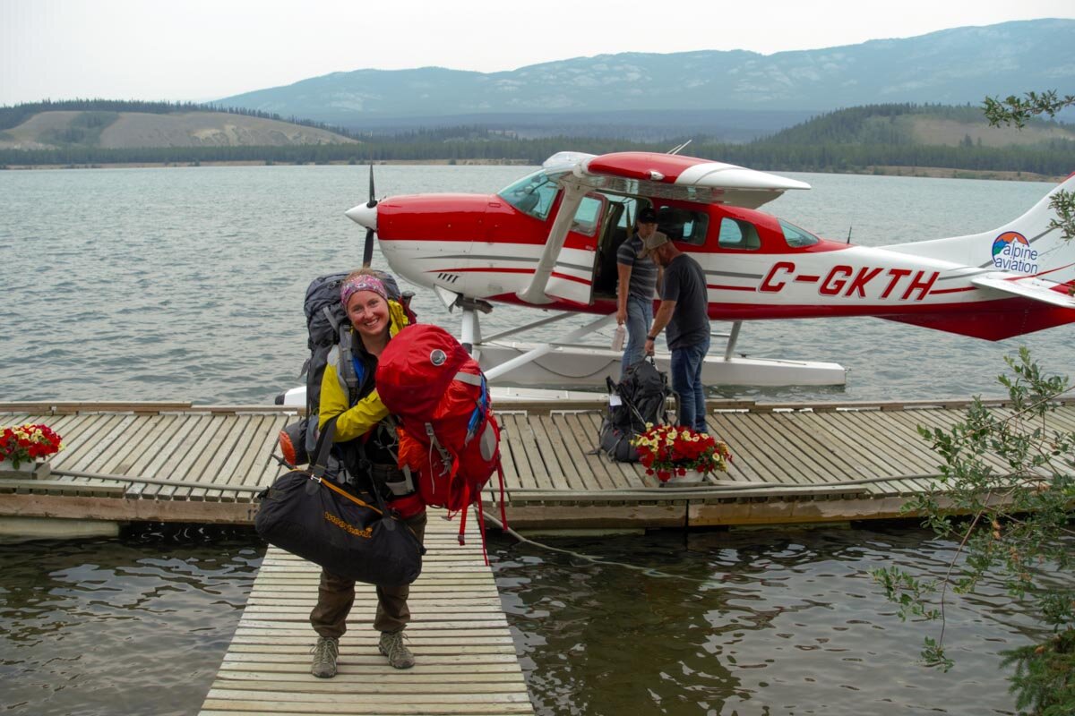 Chloe carrying clients backpacks from the float plane after Chilkoot Trail adventure
