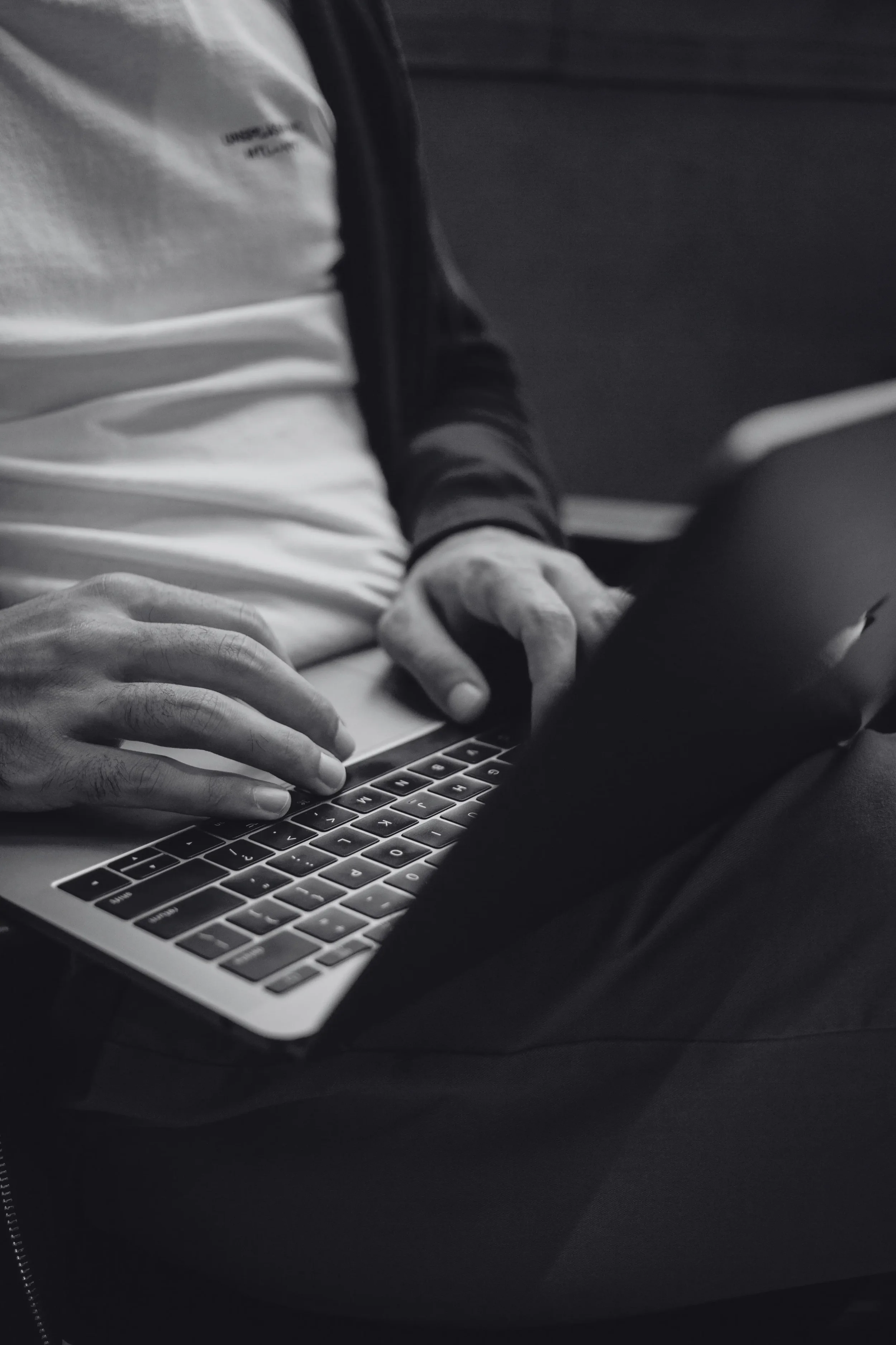 Person using a laptop, focusing on hands typing on keyboard in black and white.