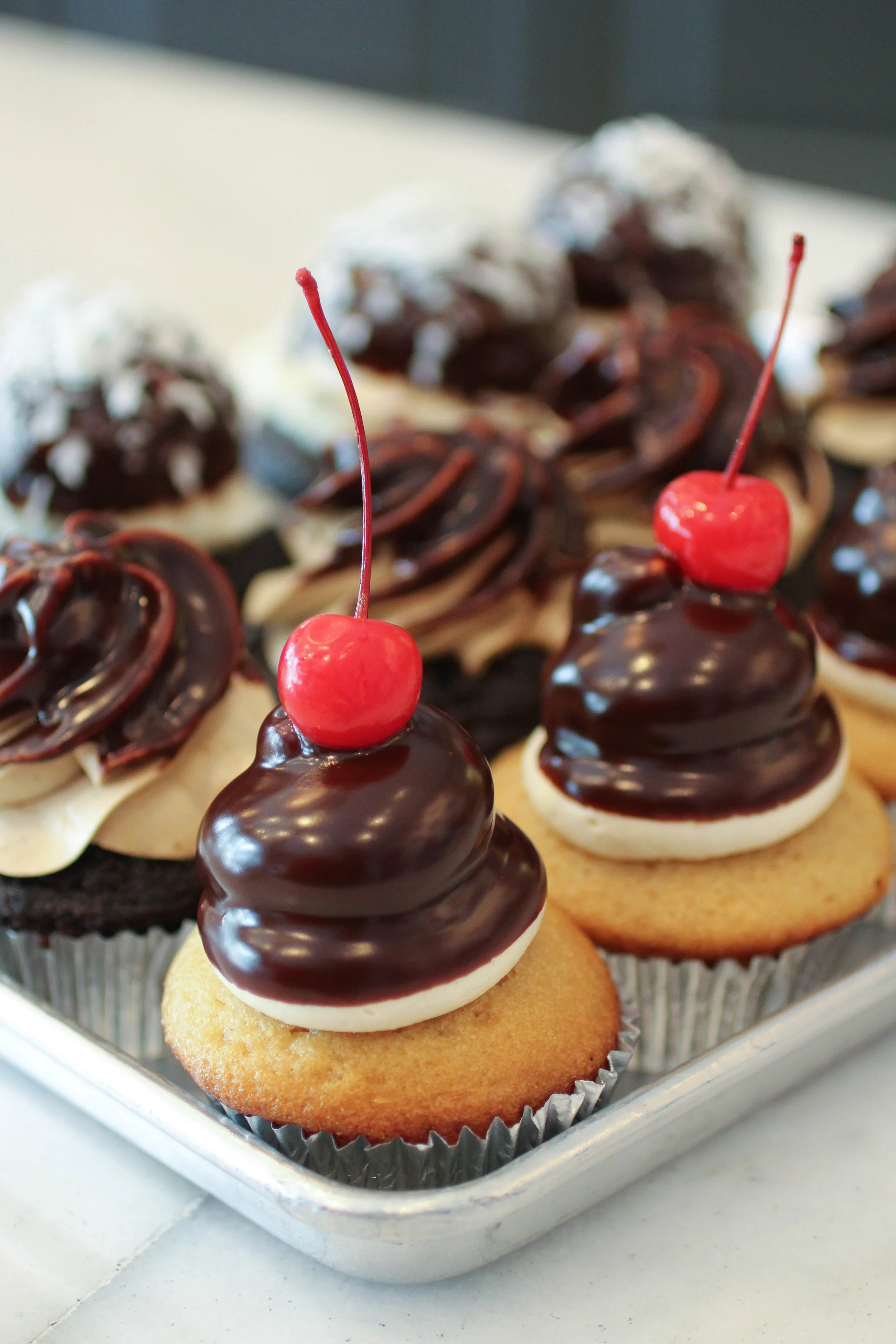 "Boss" by IveyCake - a custard filled vanilla cupcake with an eclair frosting, dipped in ganache and topped with a cherry. 