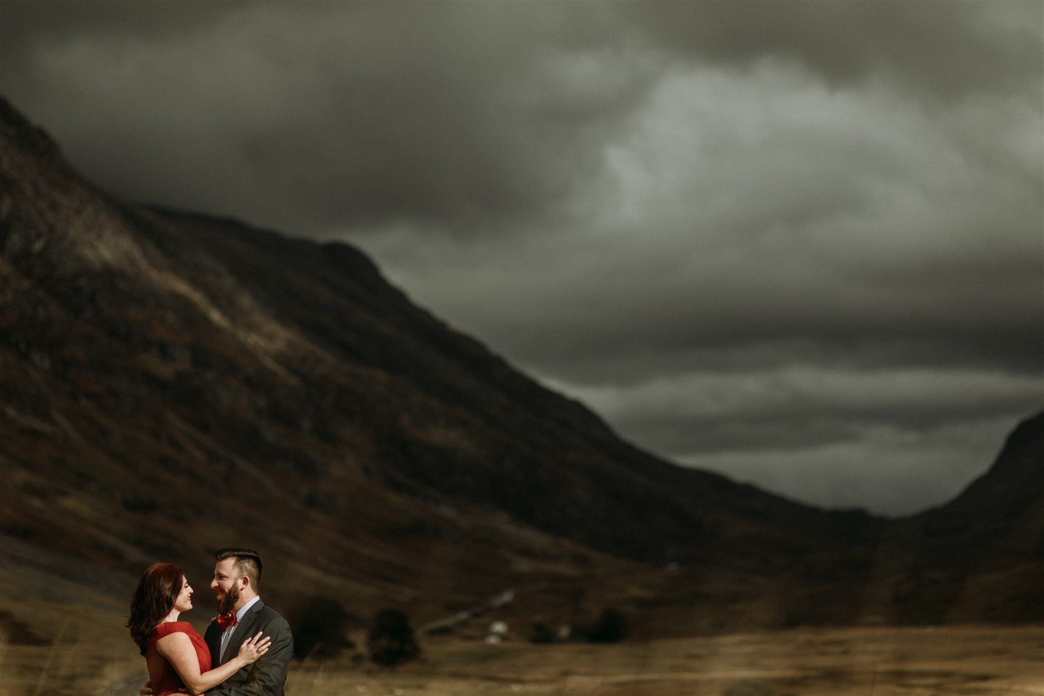 Glen Coe Scotland elopement. Bride in red dress with her groom in a field in front of mountains | Adventure elopement photographer