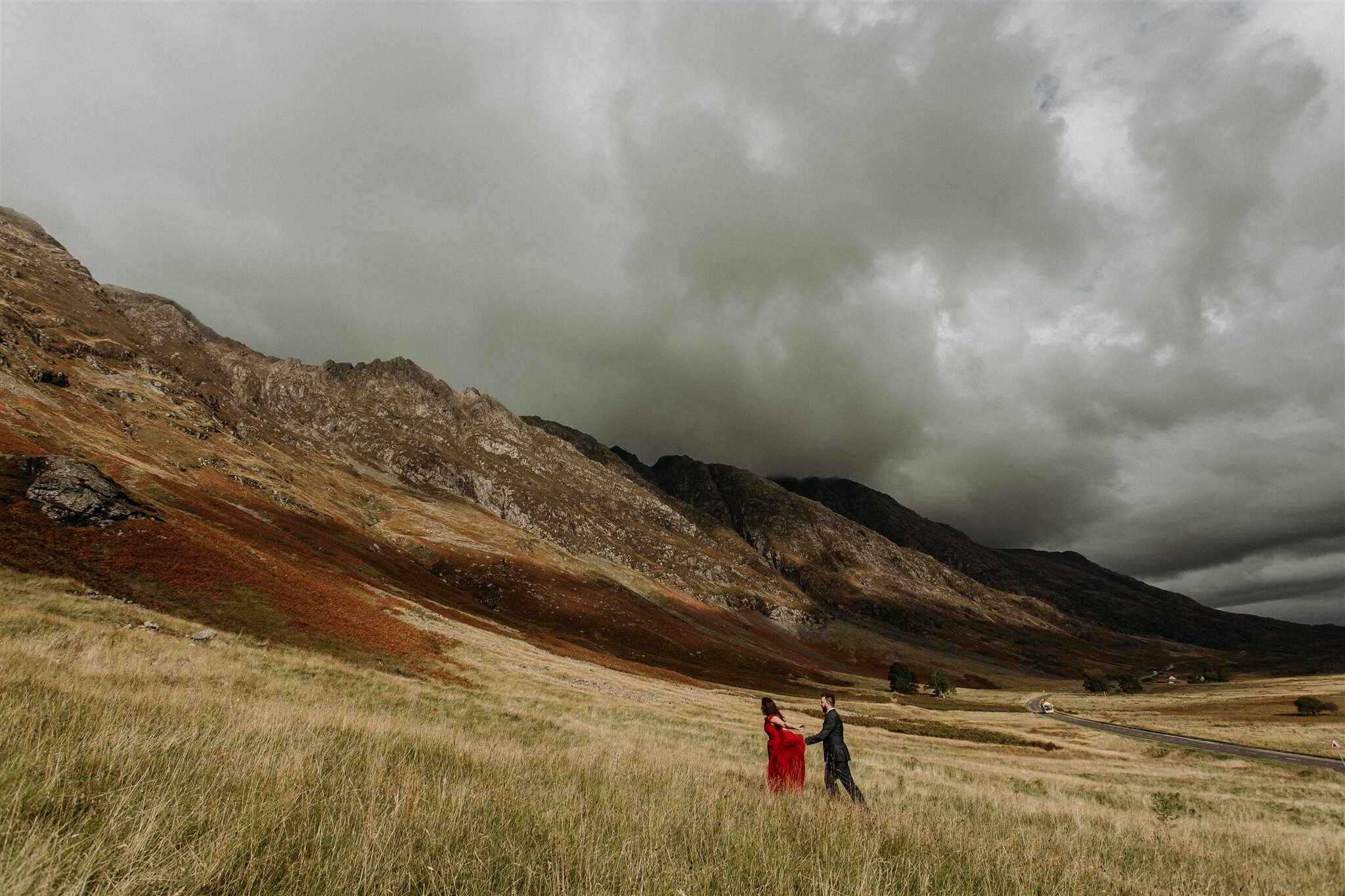 Glen Coe Scotland elopement. Bride in red dress and her groom walking through a field in the Scottish Highlands | Adventure elopement photographer