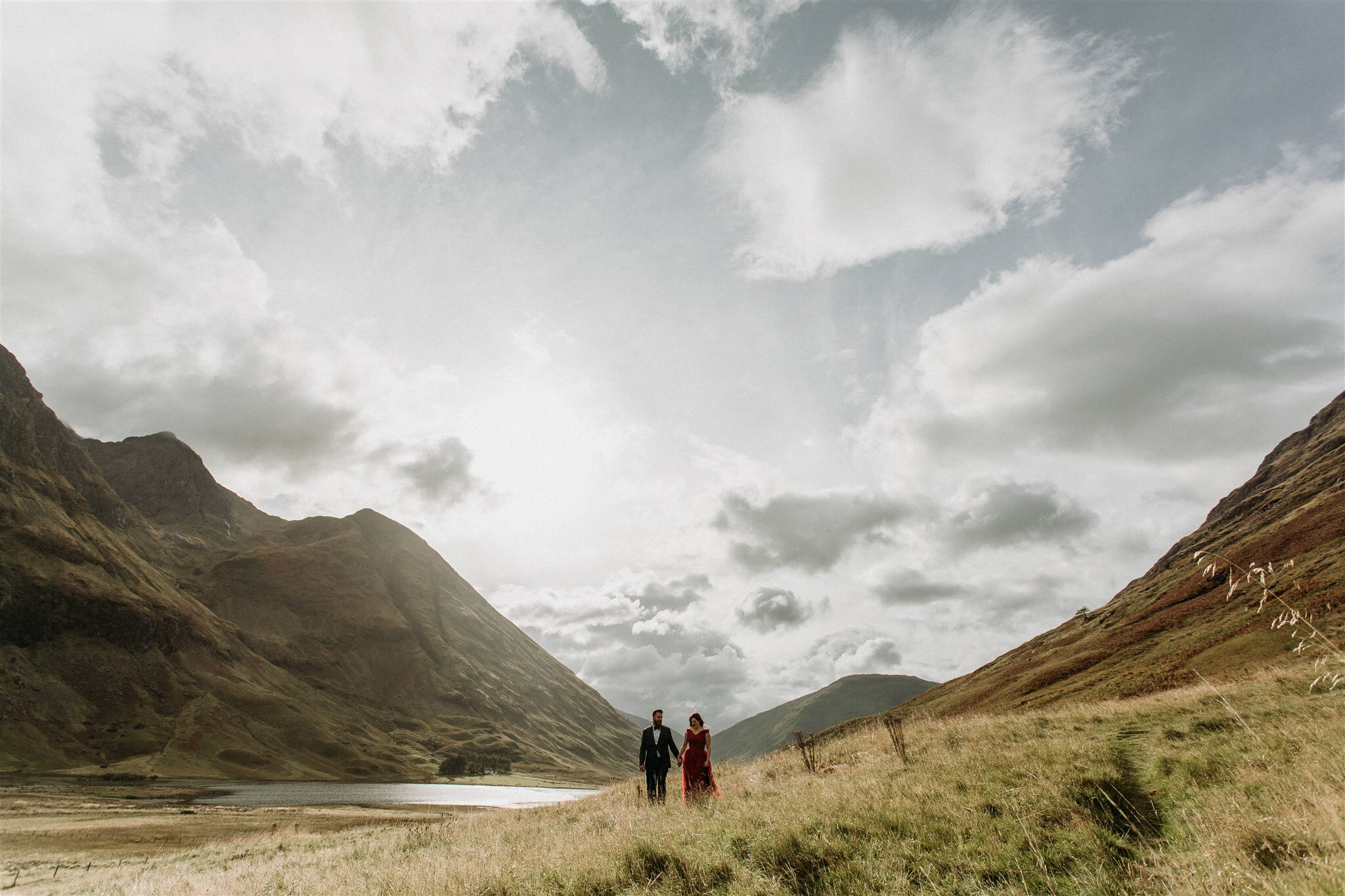 Glen Coe Scotland elopement. Bride in red dress and her groom standing side by side in a field in the Scottish Highlands | Adventure elopement photographer
