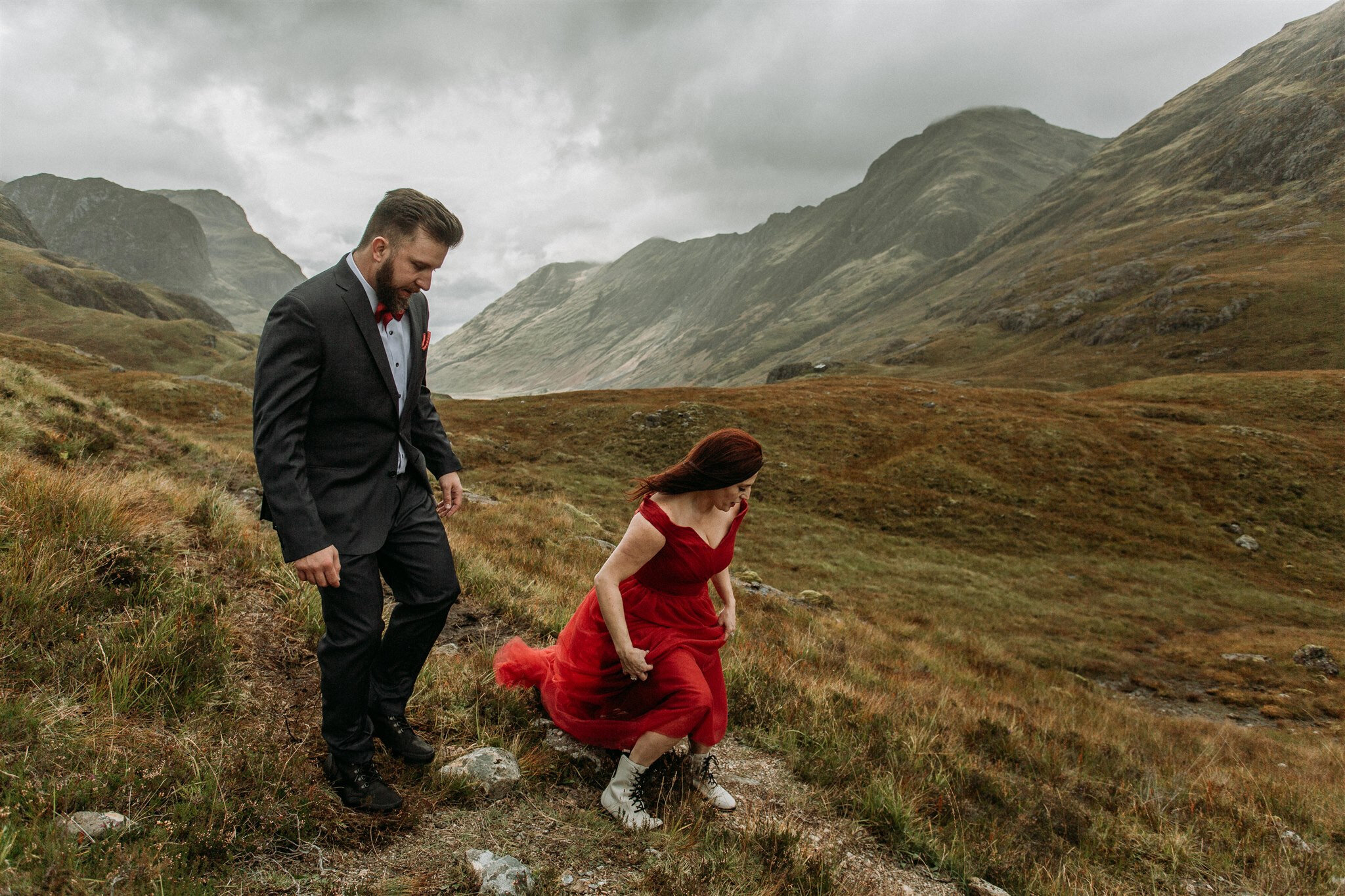 Glen Coe Scotland adventure elopement session. Bride in red dress and her groom walking in the windy Scottish Highlands | Adventure elopement photographer