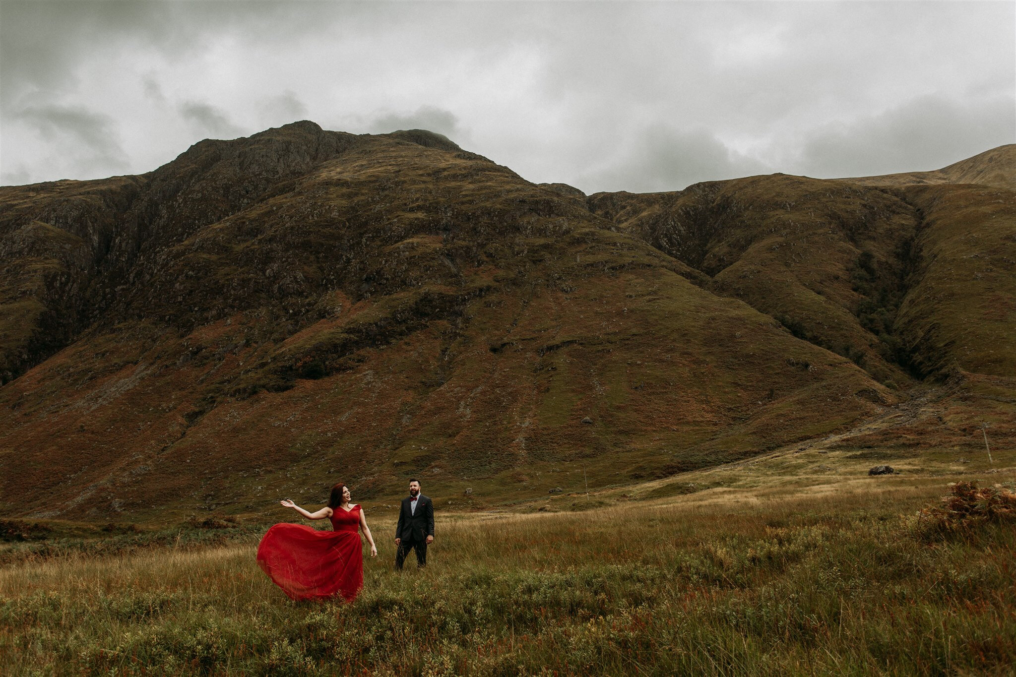 Glen Coe Scotland adventure elopement. Bride in red dress blowing in the wind stands beside her groom in the Scottish Highlands | Adventure elopement photographer