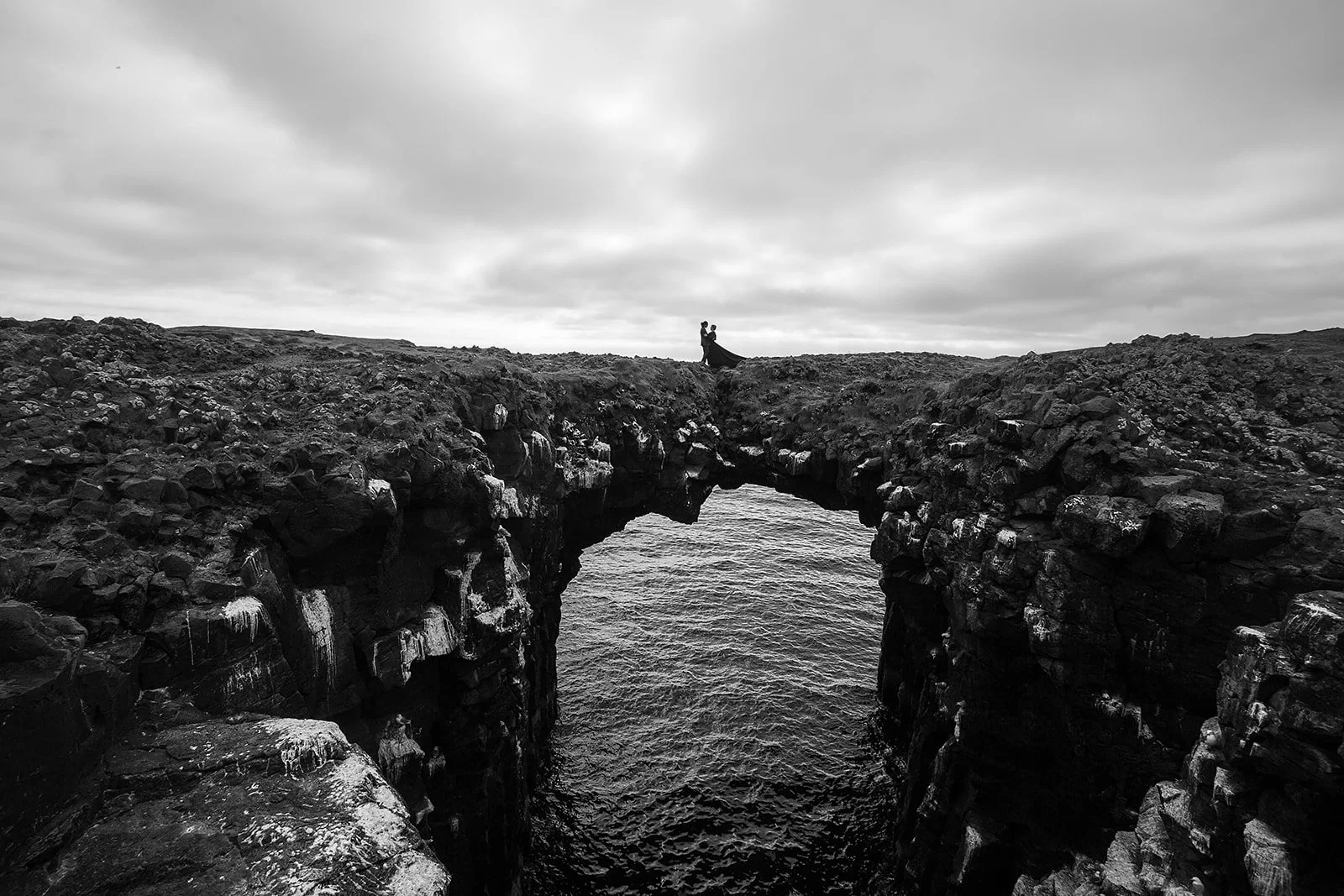 Alternative Iceland elopement couple wearing black wedding dress and purple hair — couple portraits sea cliffs Snæfellsnes rock bridge