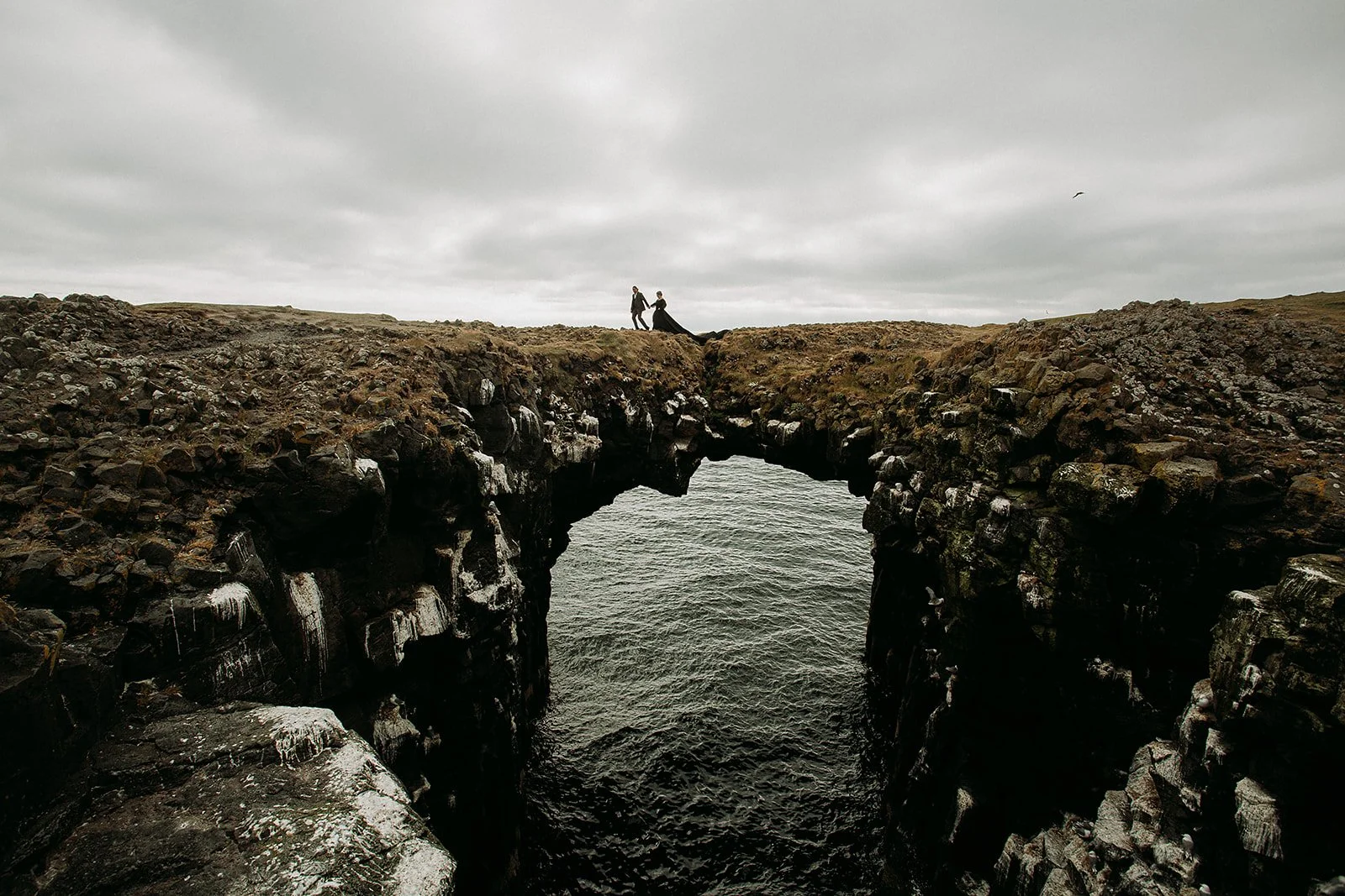 Alternative Iceland elopement couple wearing black wedding dress and purple hair — couple portraits sea cliffs Snæfellsnes rock bridge