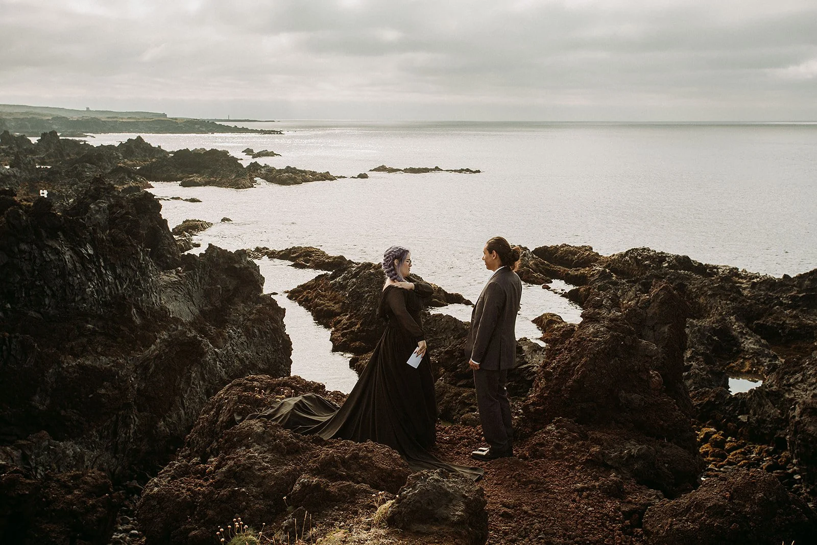 Alternative Iceland elopement couple wearing black wedding dress and purple hair — couple saying vows wedding ceremony