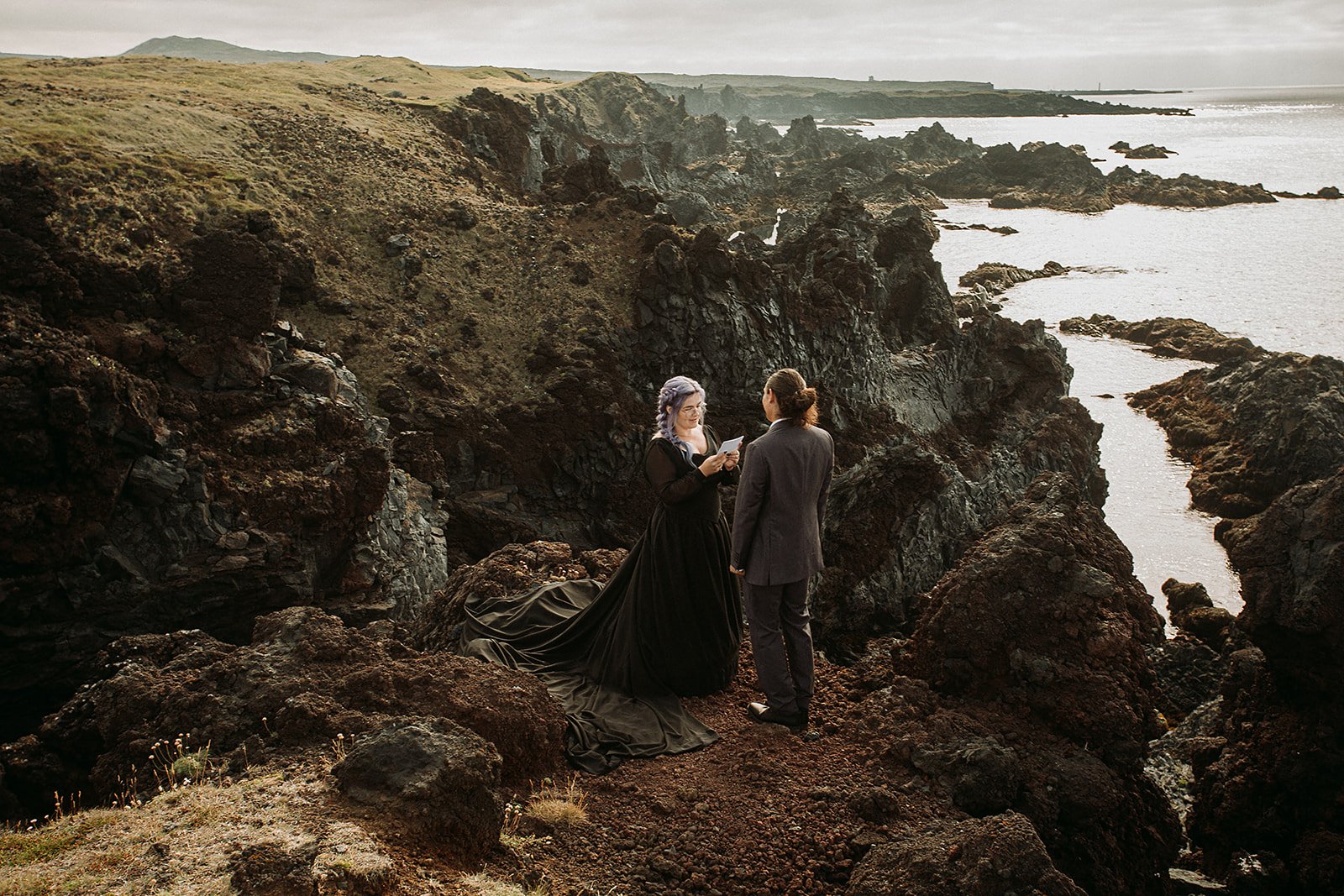Alternative Iceland elopement couple wearing black wedding dress and purple hair — couple saying vows wedding ceremony