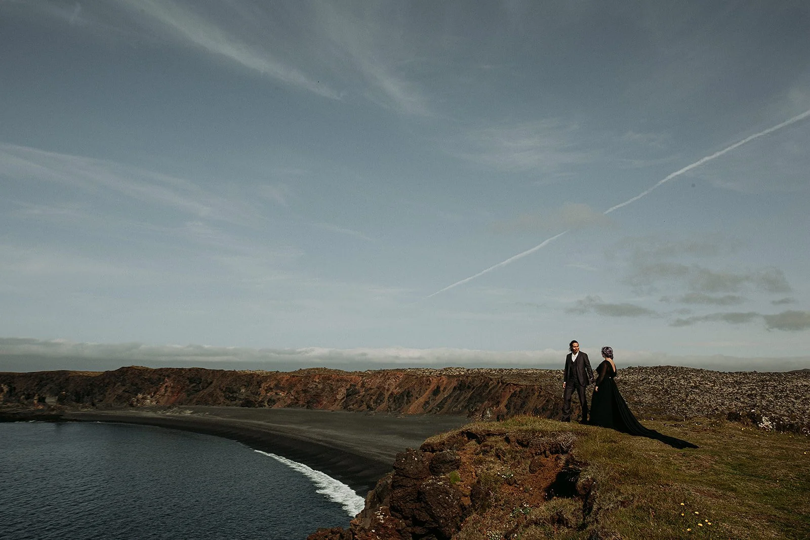 Alternative Iceland elopement couple wearing black wedding dress and purple hair — couple portraits at black sand beach