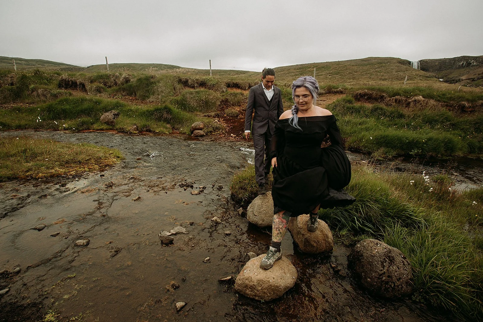 Alternative Iceland elopement couple wearing black wedding dress and purple hair — couple portraits at waterfall 