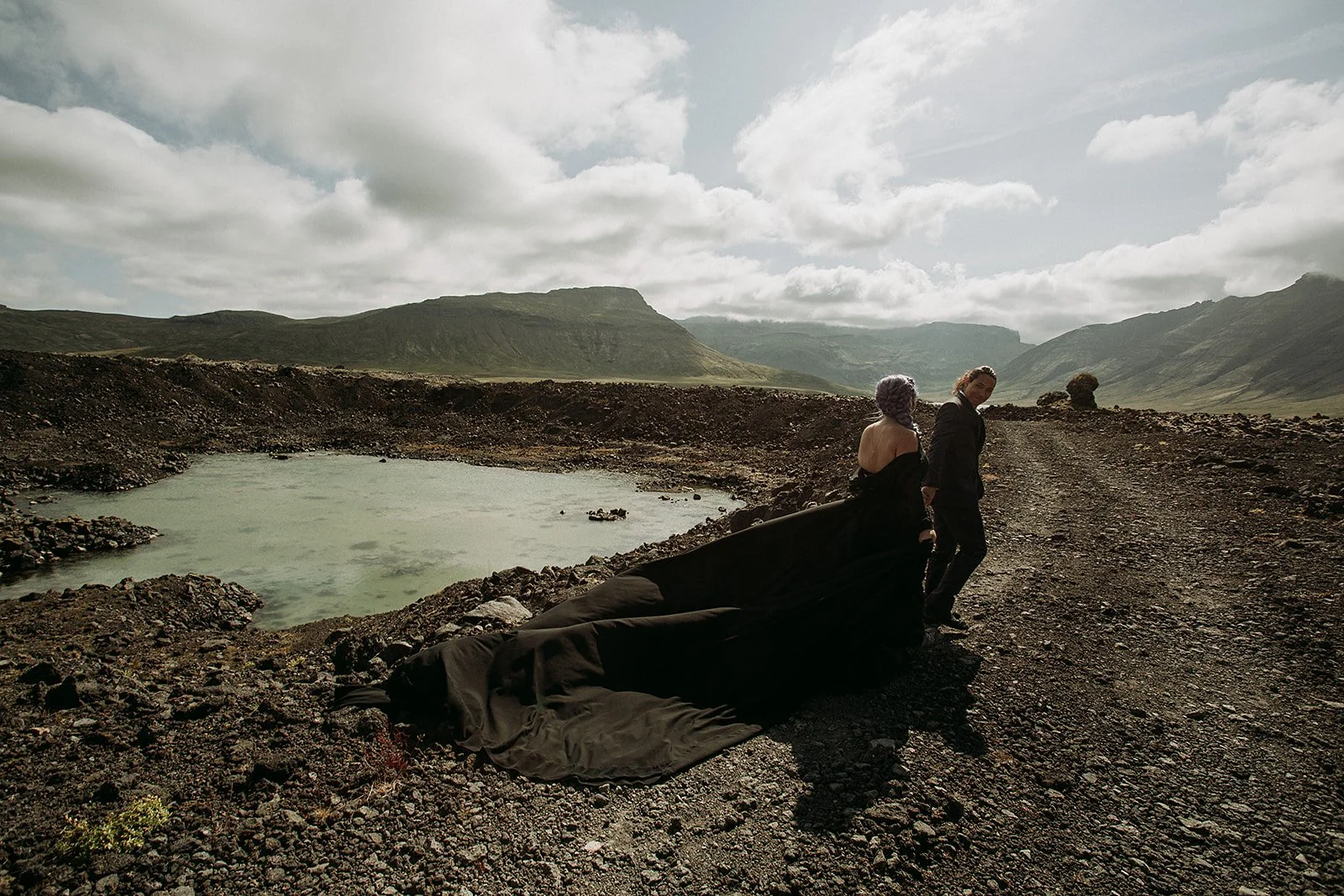 Alternative Iceland elopement couple wearing black wedding dress and purple hair — couple portraits at waterfall 