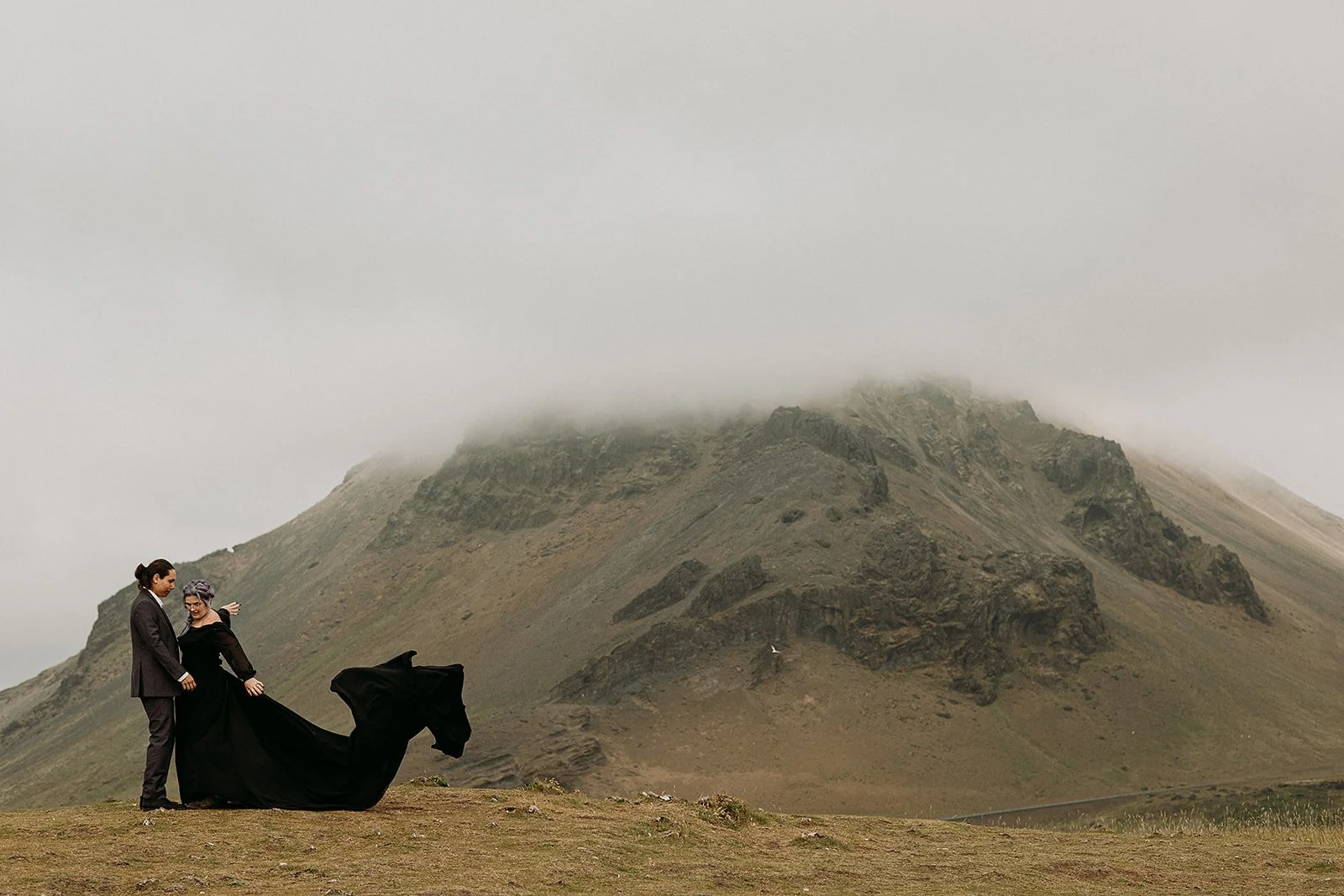 Alternative Iceland elopement couple wearing black wedding dress and purple hair — couple portraits at mountains