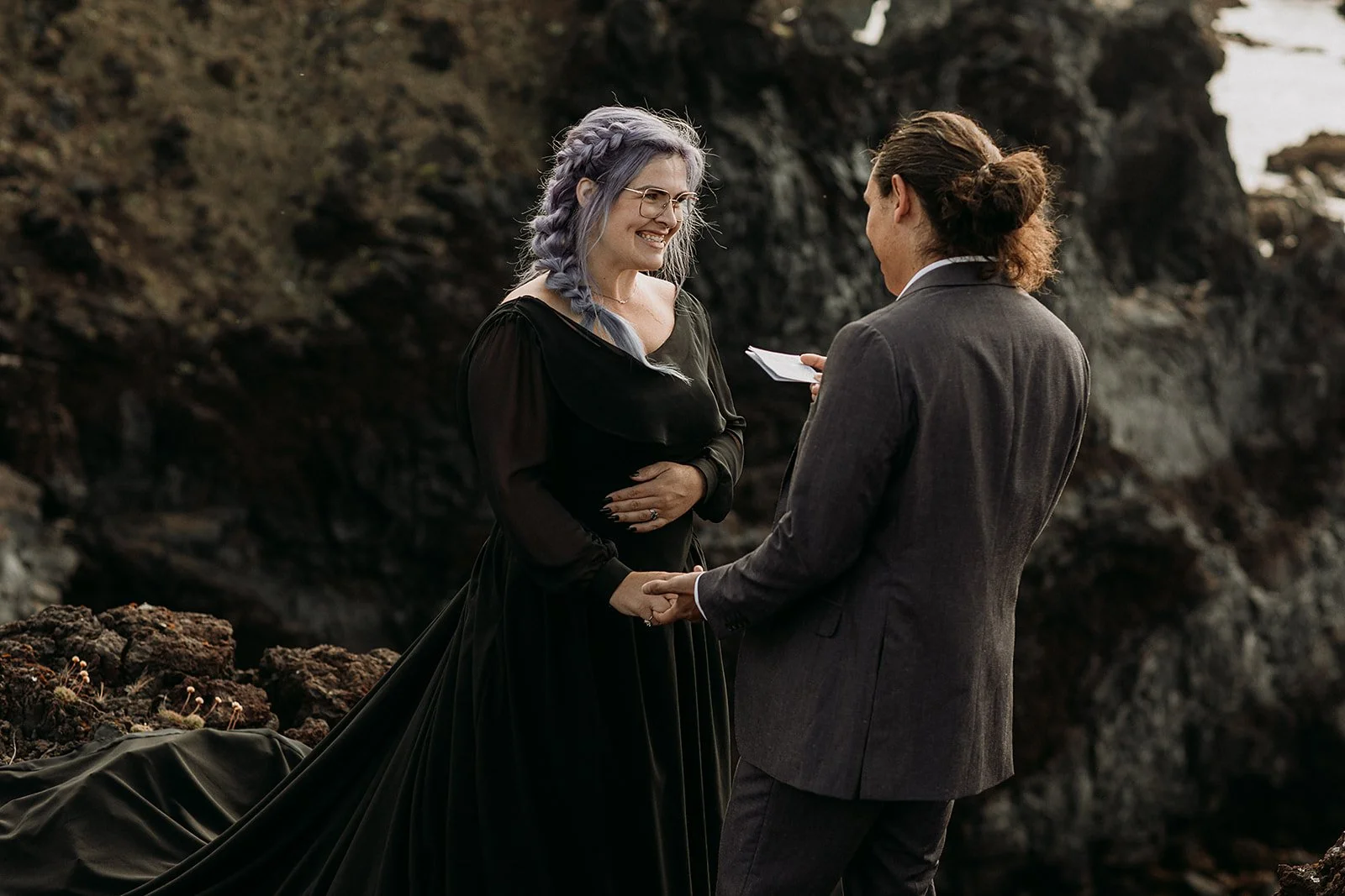 Alternative Iceland elopement couple wearing black wedding dress and purple hair — couple saying vows wedding ceremony