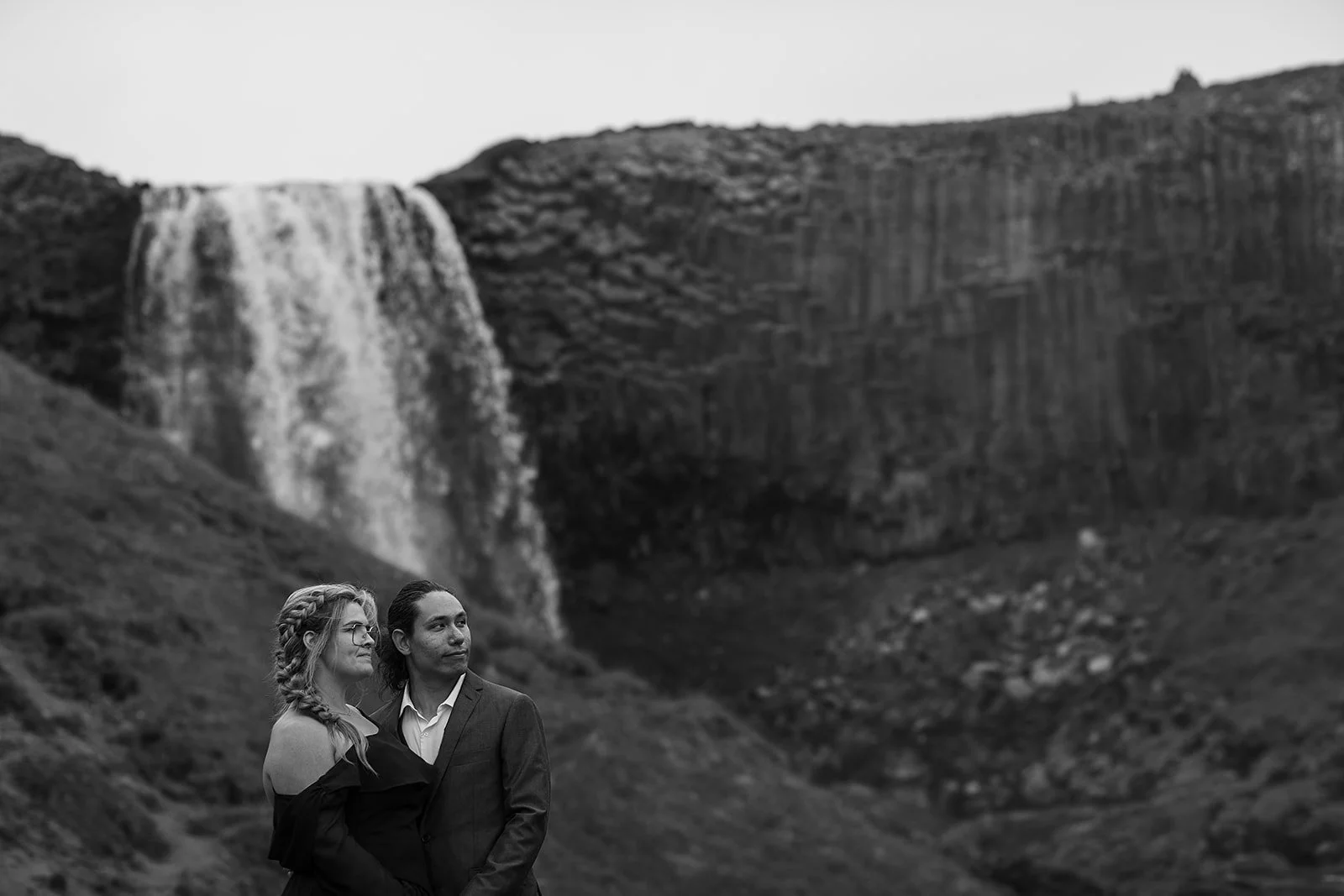 Alternative Iceland elopement couple wearing black wedding dress and purple hair — couple portraits at waterfall