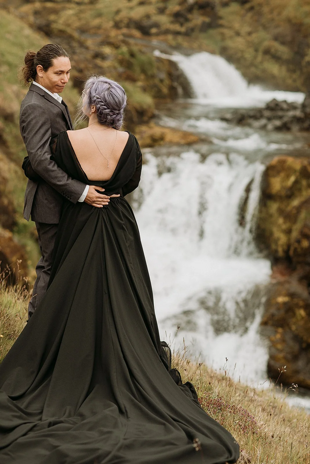 Alternative Iceland elopement couple wearing black wedding dress and purple hair — couple portraits at waterfall
