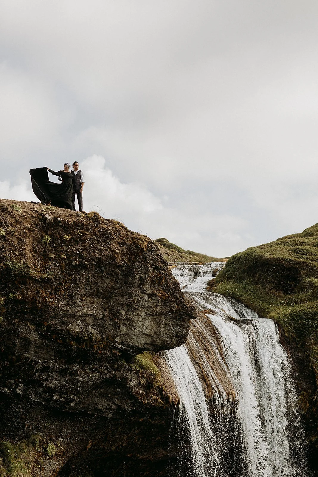 Alternative Iceland elopement couple wearing black wedding dress and purple hair — couple portraits at waterfall