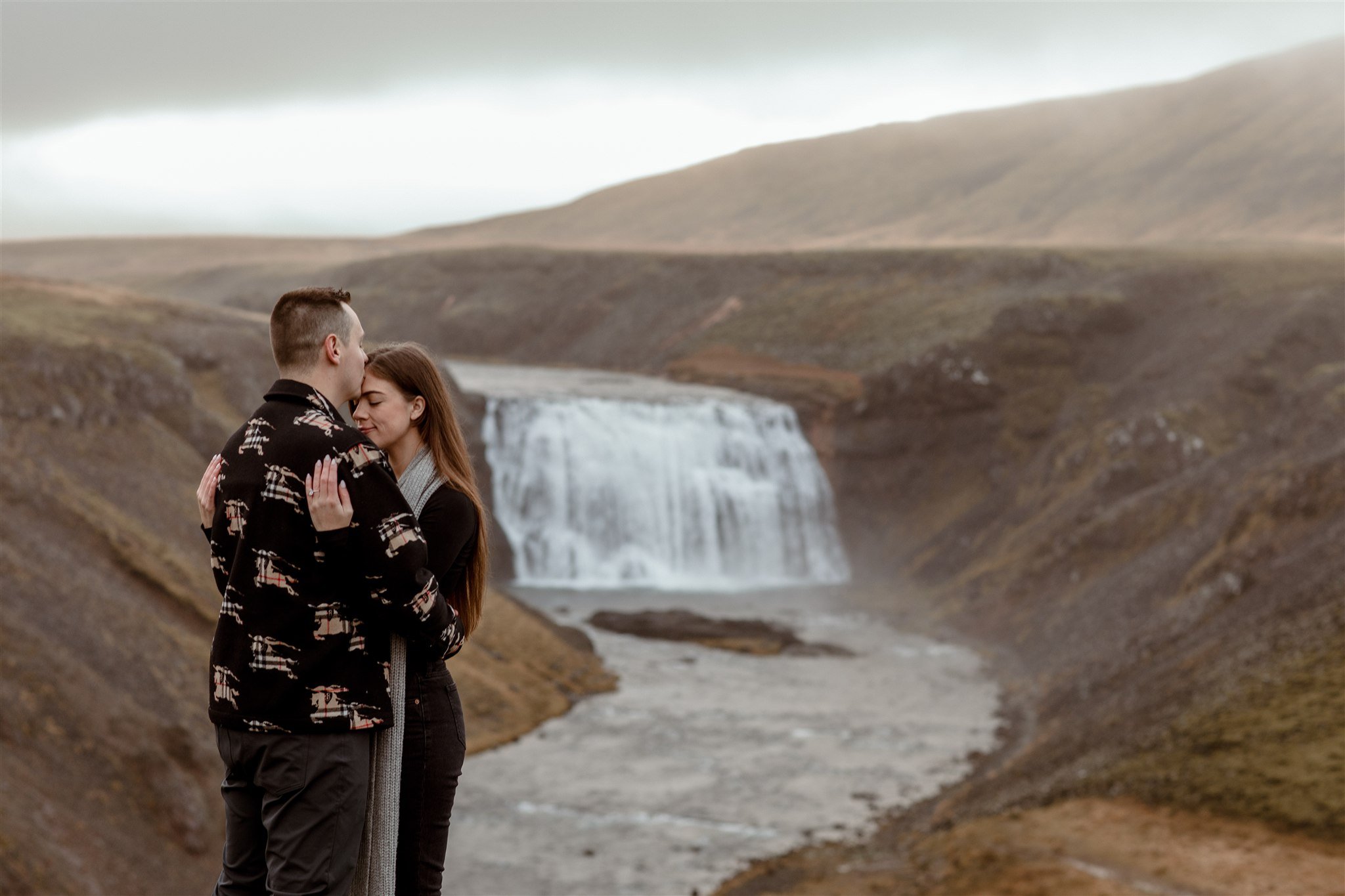 Iceland proposal at a waterfall at sunrise with the couple hugging after he proposed.