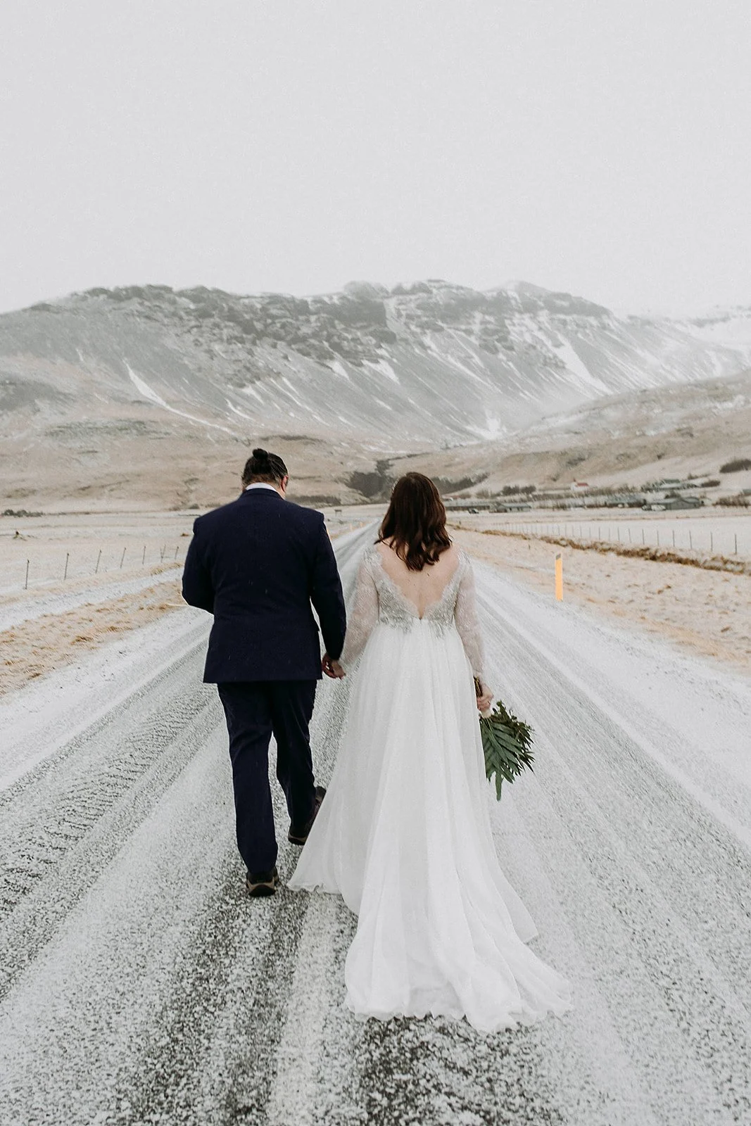 A Winter Iceland Elopement at Skógafoss (Skogafoss) and Glacier — couple in front of mountains walking down road