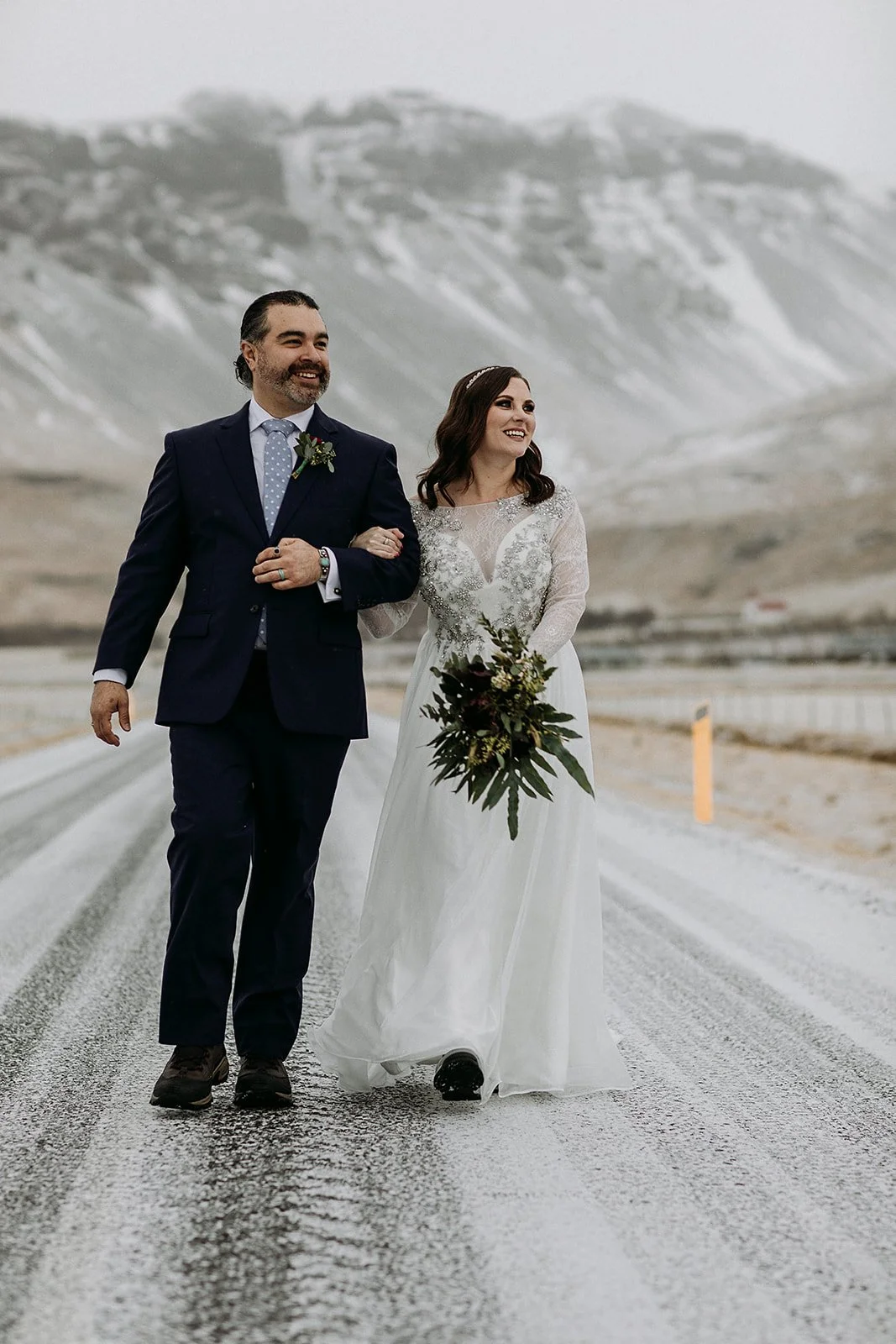 A Winter Iceland Elopement at Skógafoss (Skogafoss) and Glacier — couple in front of mountains walking down road