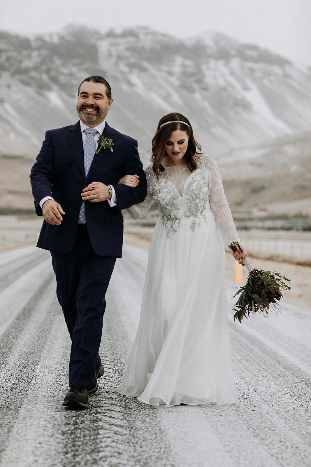 A Winter Iceland Elopement at Skógafoss (Skogafoss) and Glacier — couple in front of mountains walking down road