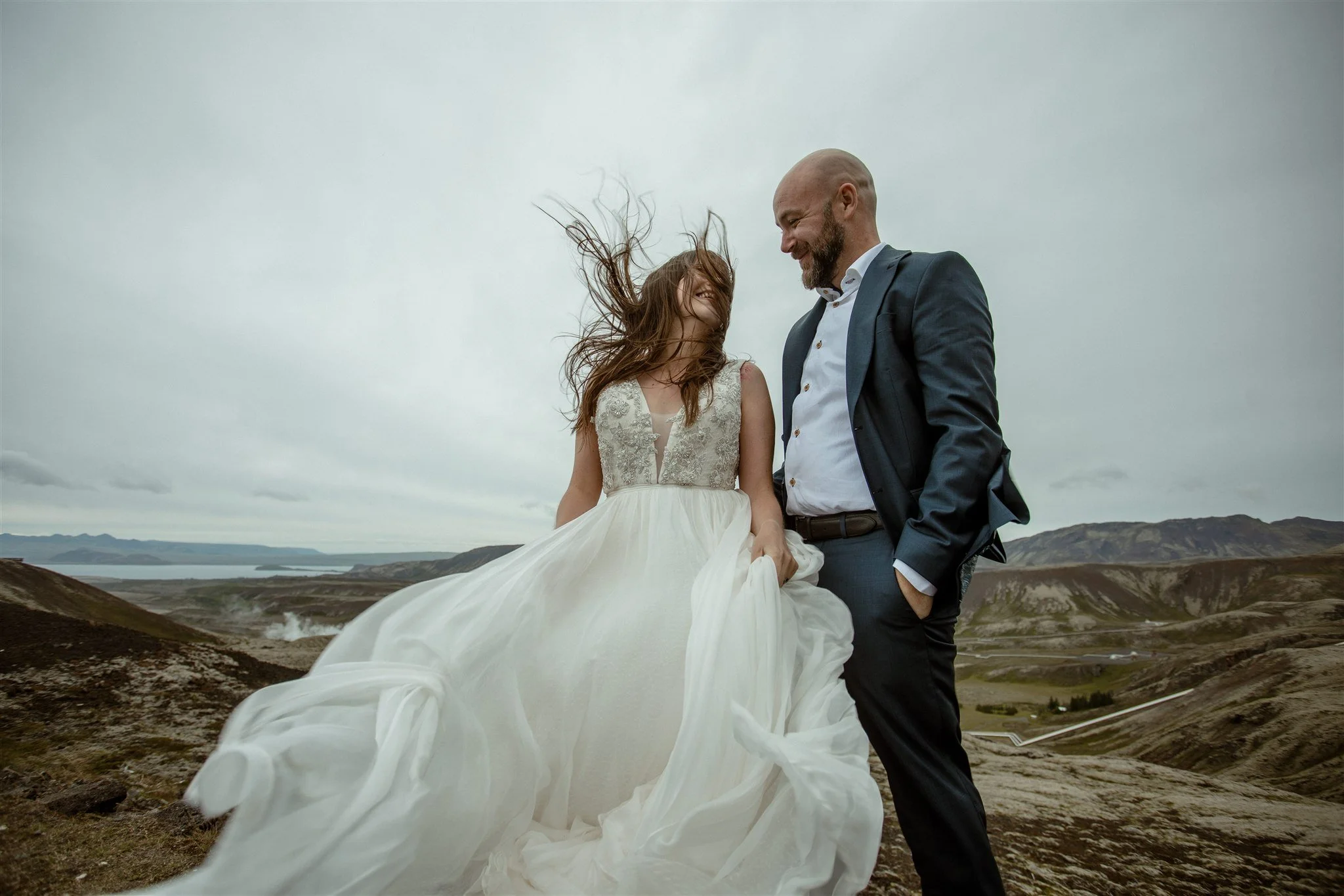  A Private Lake Iceland Elopement Starting in Reykjavík with Guests by Iceland elopement photographer &amp; planner Steph Zakas — couple on an adventure for elopement photos at a volcanic area with wind 