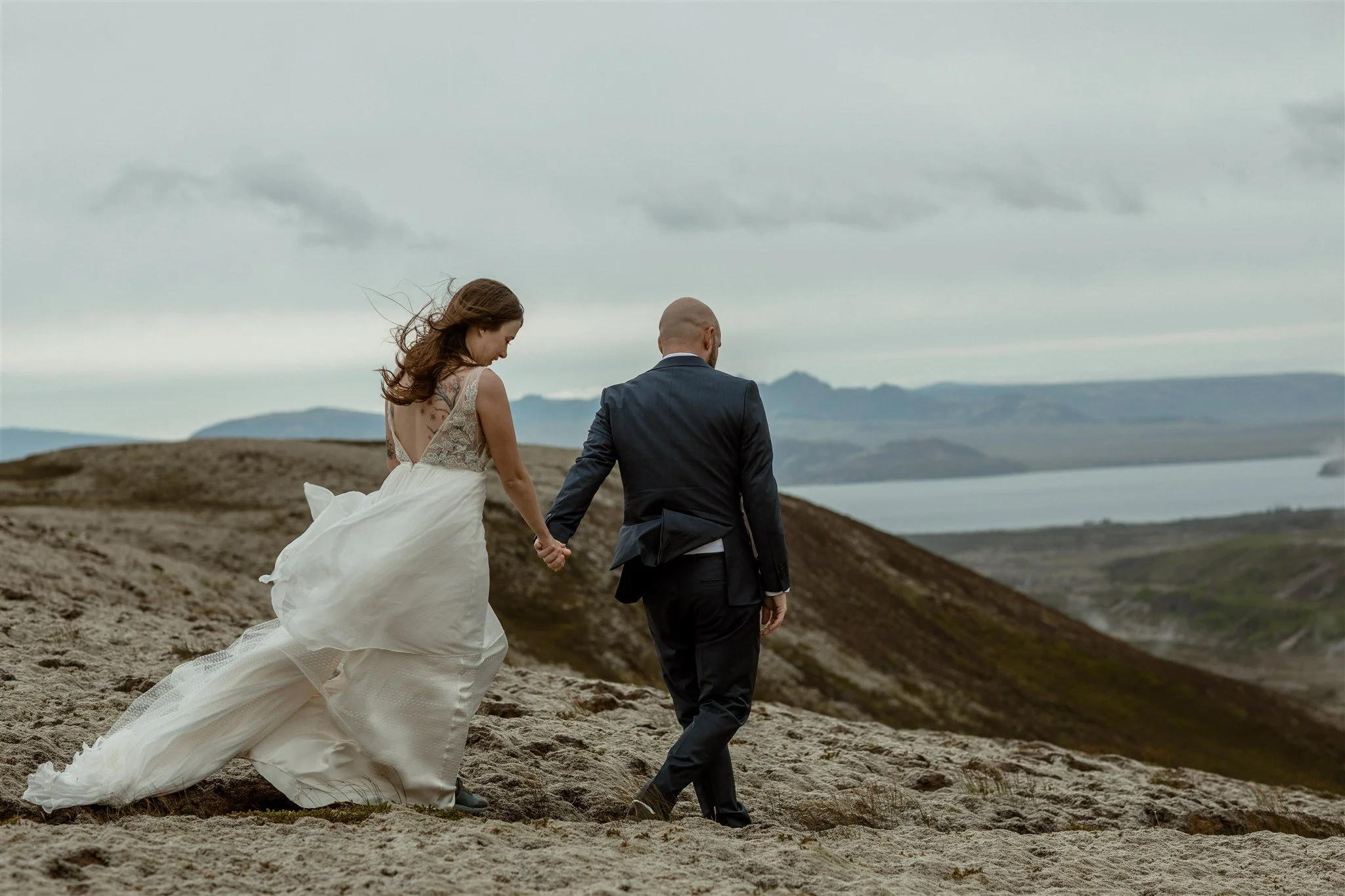  A Private Lake Iceland Elopement Starting in Reykjavík with Guests by Iceland elopement photographer &amp; planner Steph Zakas — couple on an adventure for elopement photos at a volcanic area with wind 