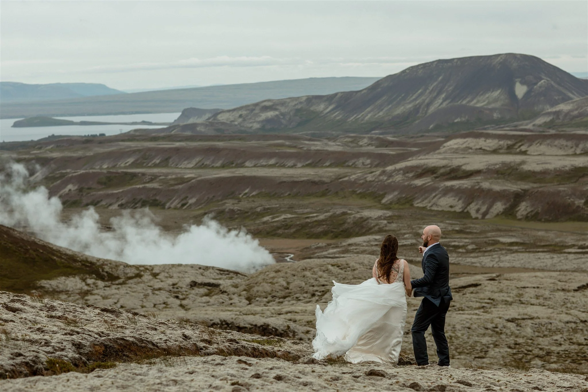  A Private Lake Iceland Elopement Starting in Reykjavík with Guests by Iceland elopement photographer &amp; planner Steph Zakas — couple on an adventure for elopement photos at a volcanic area with wind 