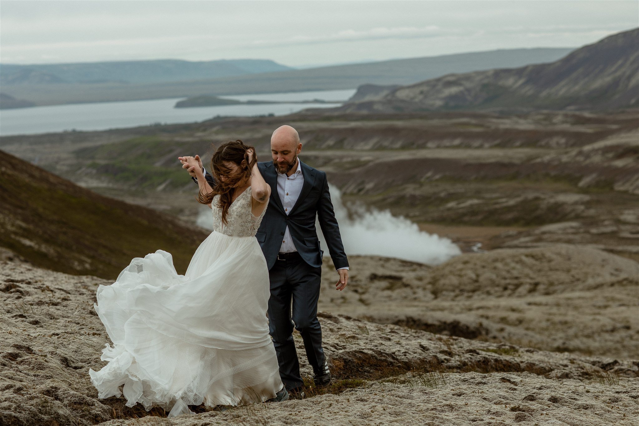  A Private Lake Iceland Elopement Starting in Reykjavík with Guests by Iceland elopement photographer &amp; planner Steph Zakas — couple on an adventure for elopement photos at a volcanic area with wind 