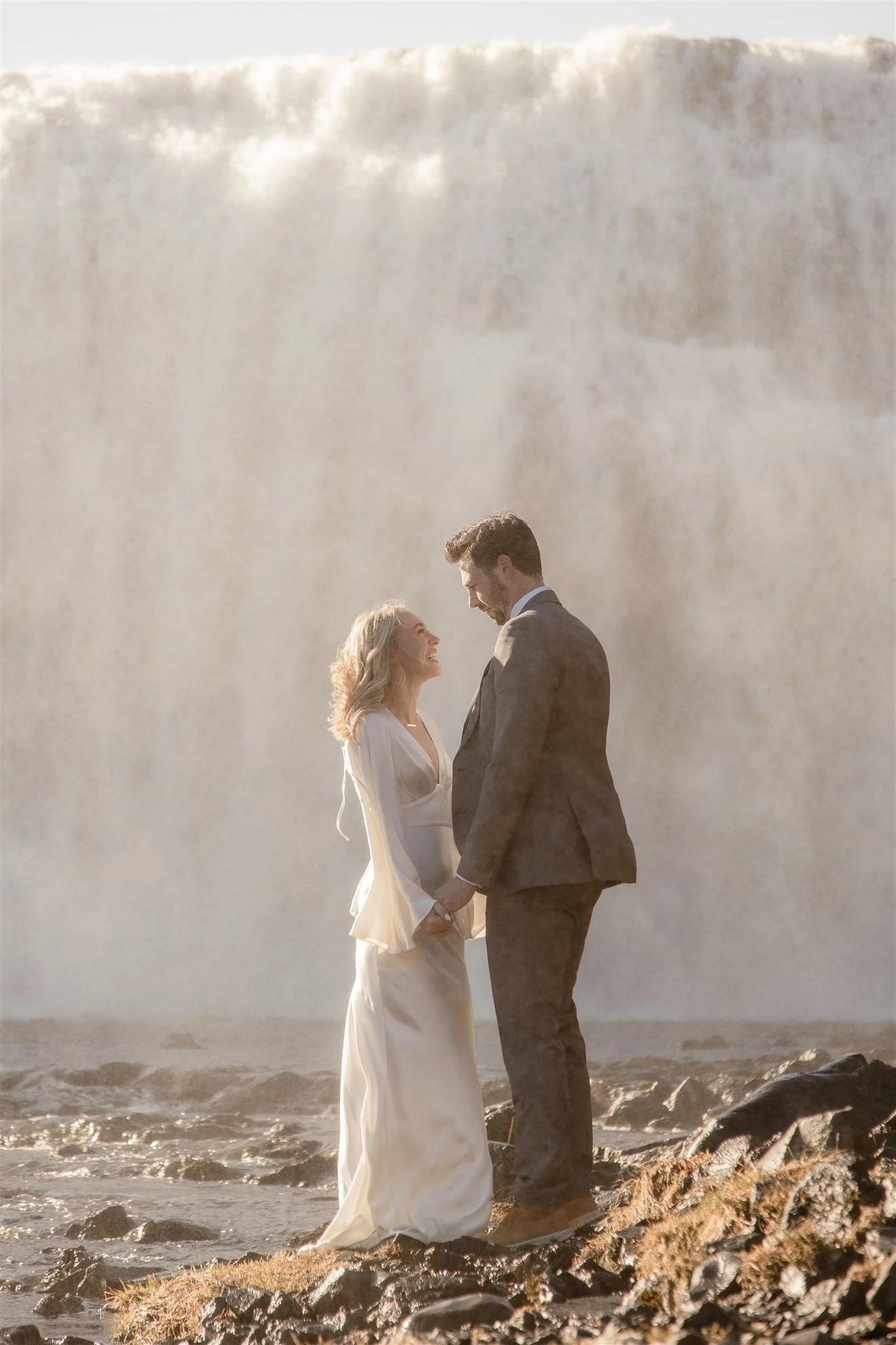 Lord of the Rings Inspired Iceland Engagement Photoshoot at waterfall — couple standing together with Arwen inspired dress with beautiful light and waterfall mist