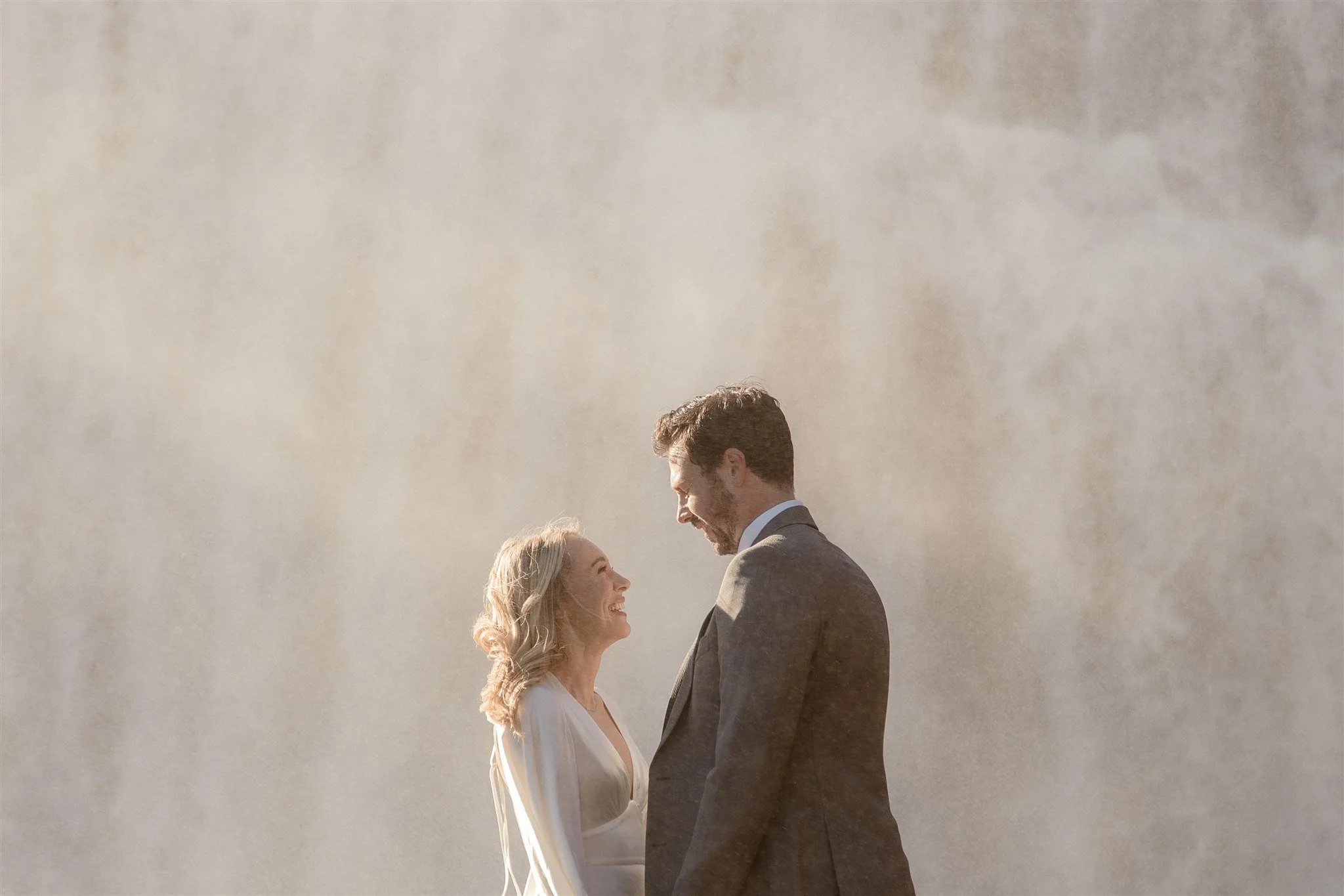 Lord of the Rings Inspired Iceland Engagement Photoshoot at waterfall — couple standing together with Arwen inspired dress with beautiful light and waterfall mist