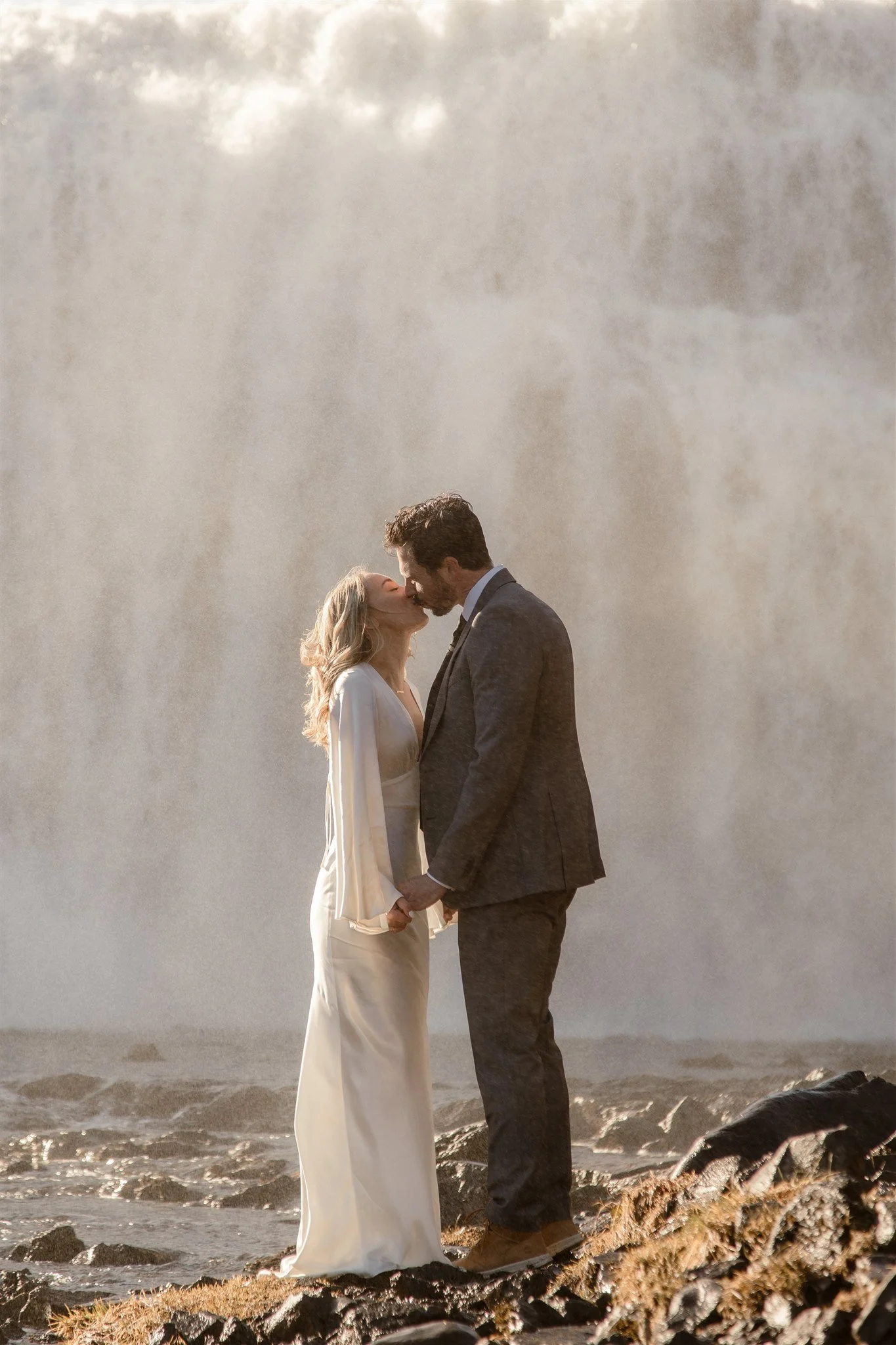 Lord of the Rings Inspired Iceland Engagement Photoshoot at waterfall — couple standing together with Arwen inspired dress with beautiful light and waterfall mist