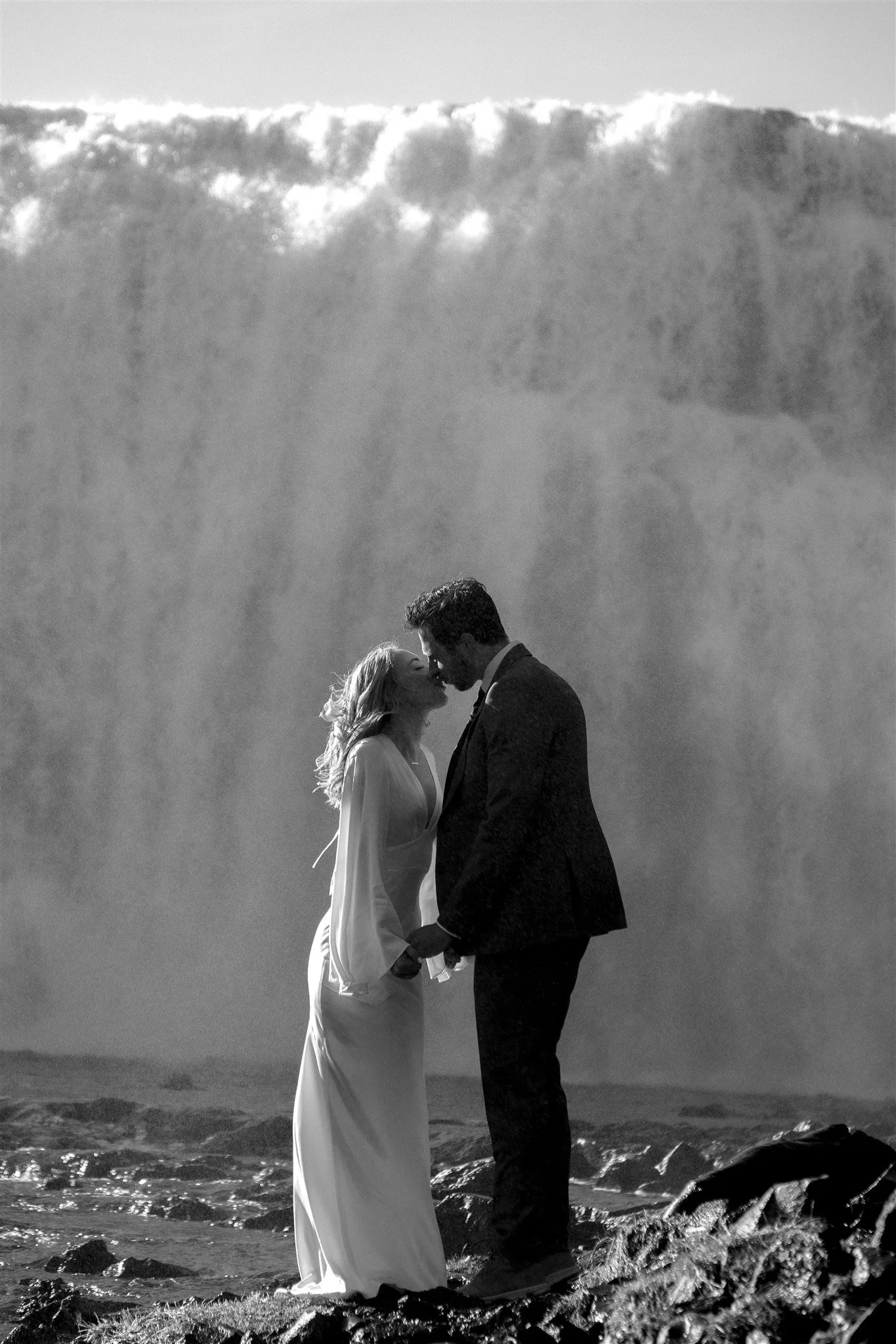 Lord of the Rings Inspired Iceland Engagement Photoshoot at waterfall — couple standing together with Arwen inspired dress with beautiful light and waterfall mist