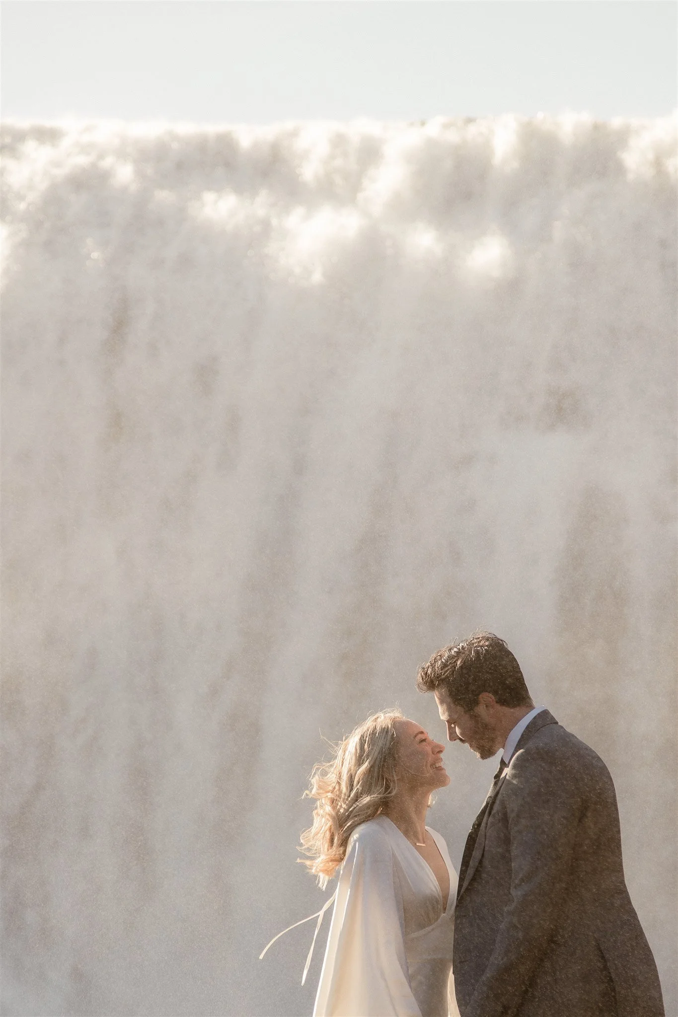 Lord of the Rings Inspired Iceland Engagement Photoshoot at waterfall — couple standing together with Arwen inspired dress with beautiful light and waterfall mist