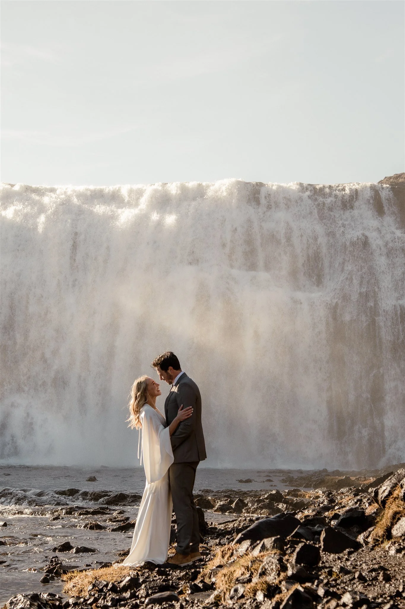 Lord of the Rings Inspired Iceland Engagement Photoshoot at waterfall — couple standing together with Arwen inspired dress with beautiful light and waterfall mist