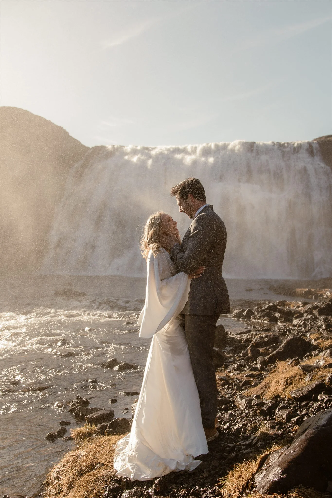 Lord of the Rings Inspired Iceland Engagement Photoshoot at waterfall — couple standing together with Arwen inspired dress with beautiful light and waterfall mist