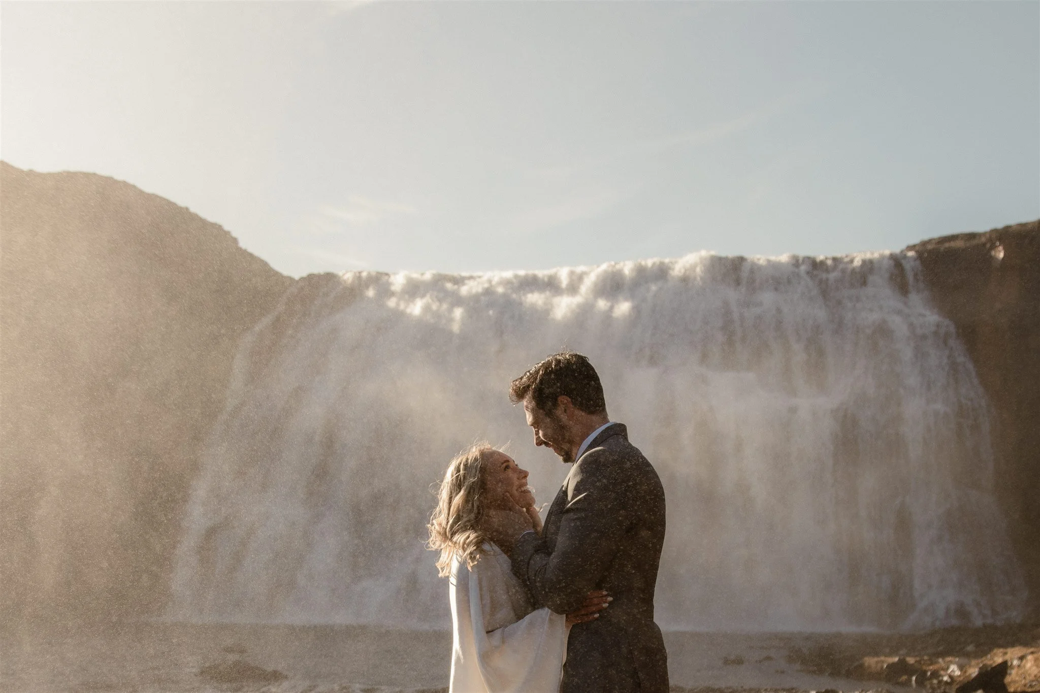 Lord of the Rings Inspired Iceland Engagement Photoshoot at waterfall — couple standing together with Arwen inspired dress with beautiful light and waterfall mist