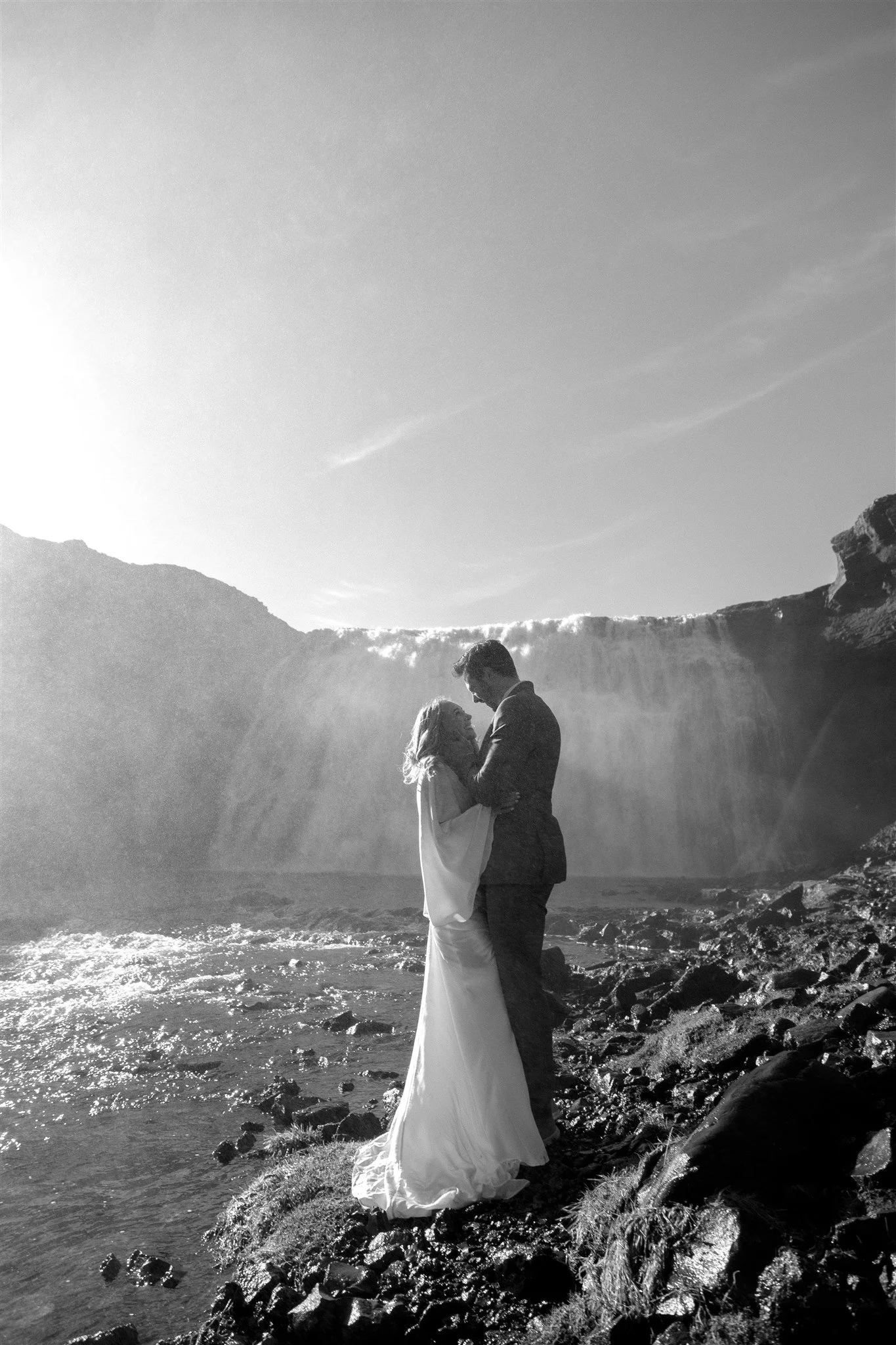 Lord of the Rings Inspired Iceland Engagement Photoshoot at waterfall — couple standing together with Arwen inspired dress with beautiful light and waterfall mist
