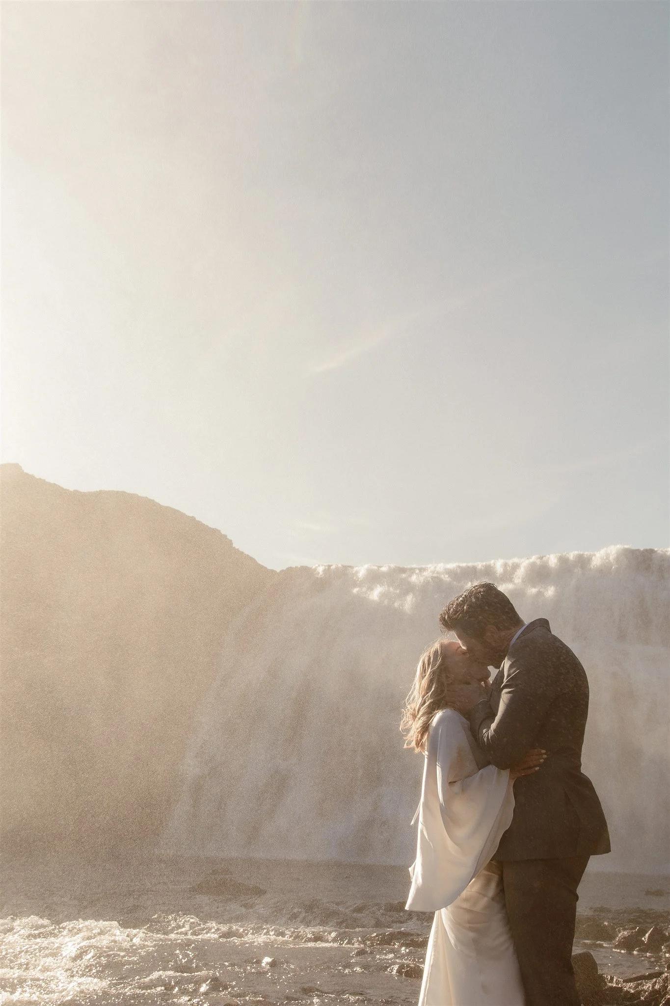 Lord of the Rings Inspired Iceland Engagement Photoshoot at waterfall — couple standing together with Arwen inspired dress with beautiful light and waterfall mist