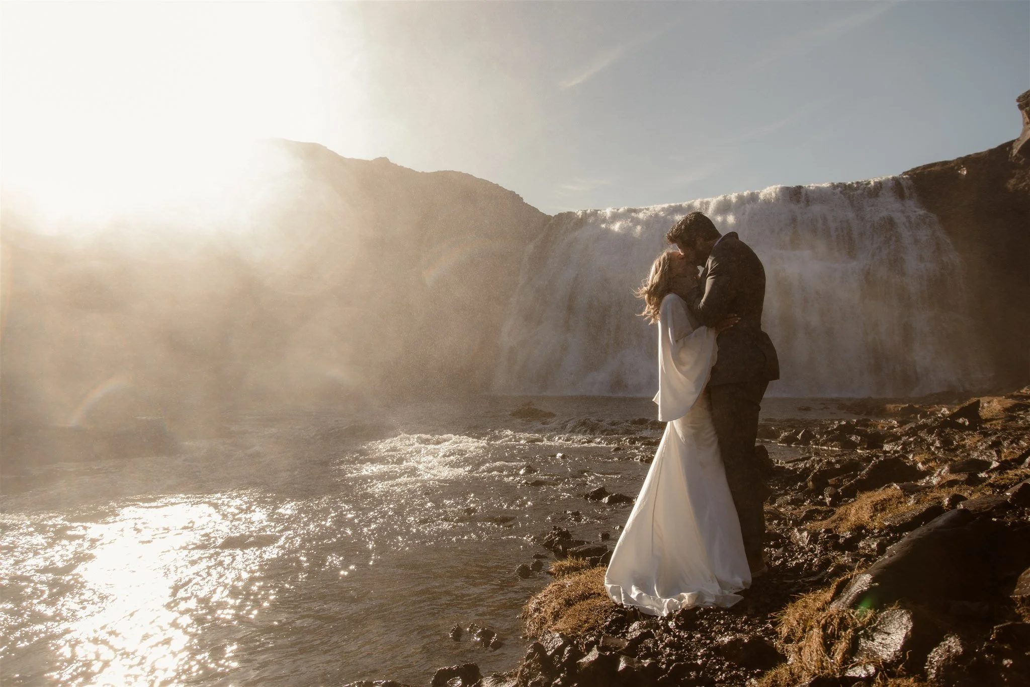 Lord of the Rings Inspired Iceland Engagement Photoshoot at waterfall — couple standing together with Arwen inspired dress with beautiful light and waterfall mist