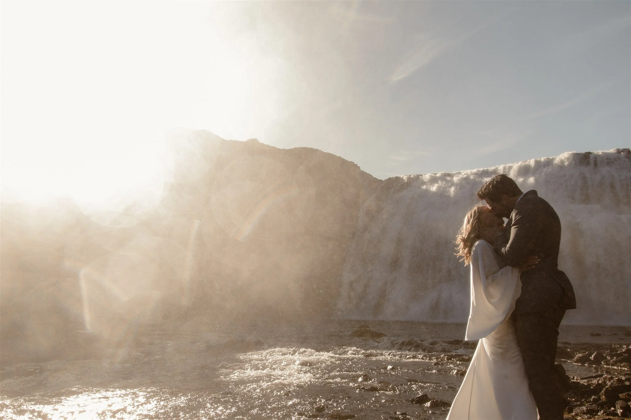 Lord of the Rings Inspired Iceland Engagement Photoshoot at waterfall — couple standing together with Arwen inspired dress with beautiful light and waterfall mist