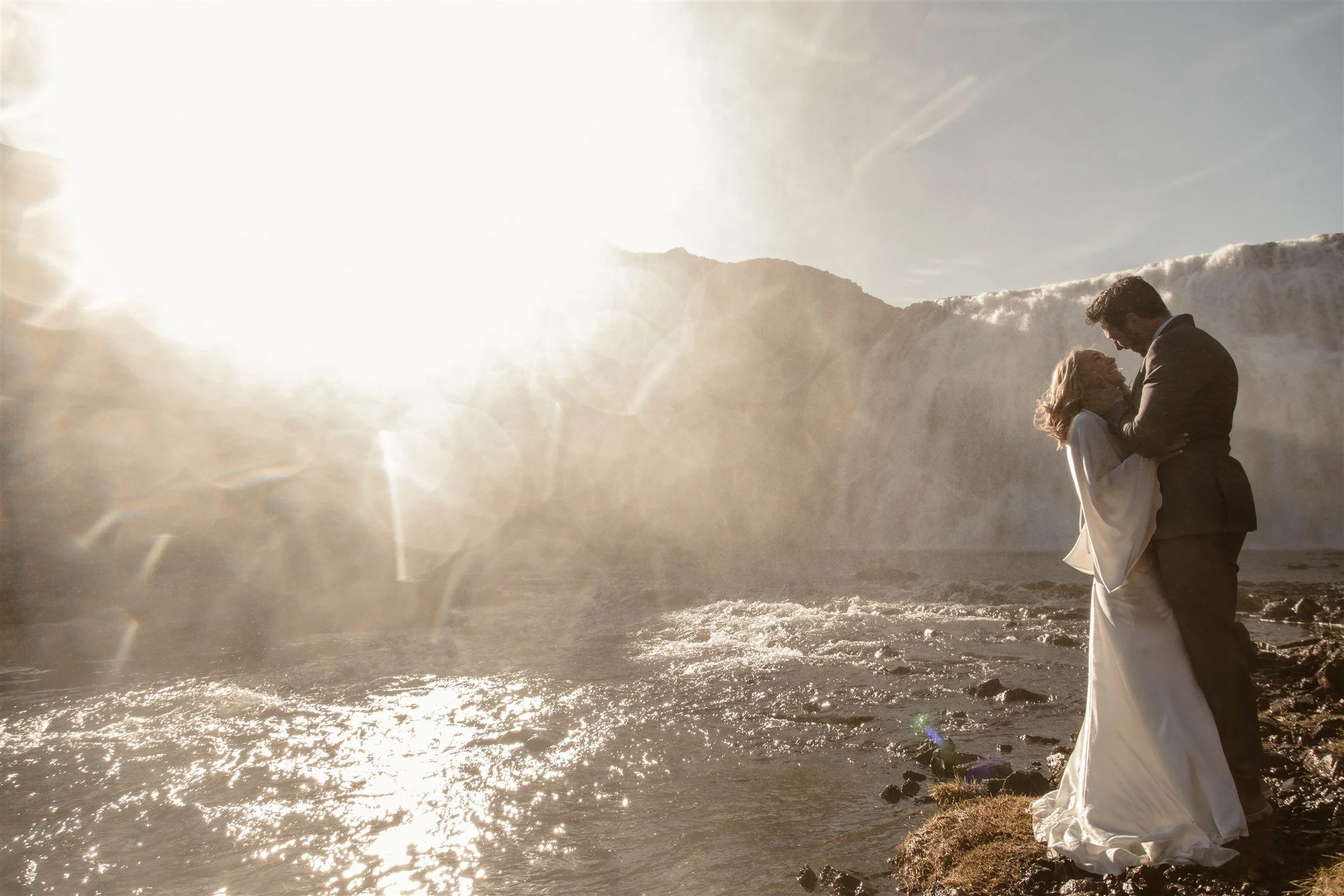 Lord of the Rings Inspired Iceland Engagement Photoshoot at waterfall — couple standing together with Arwen inspired dress with beautiful light and waterfall mist