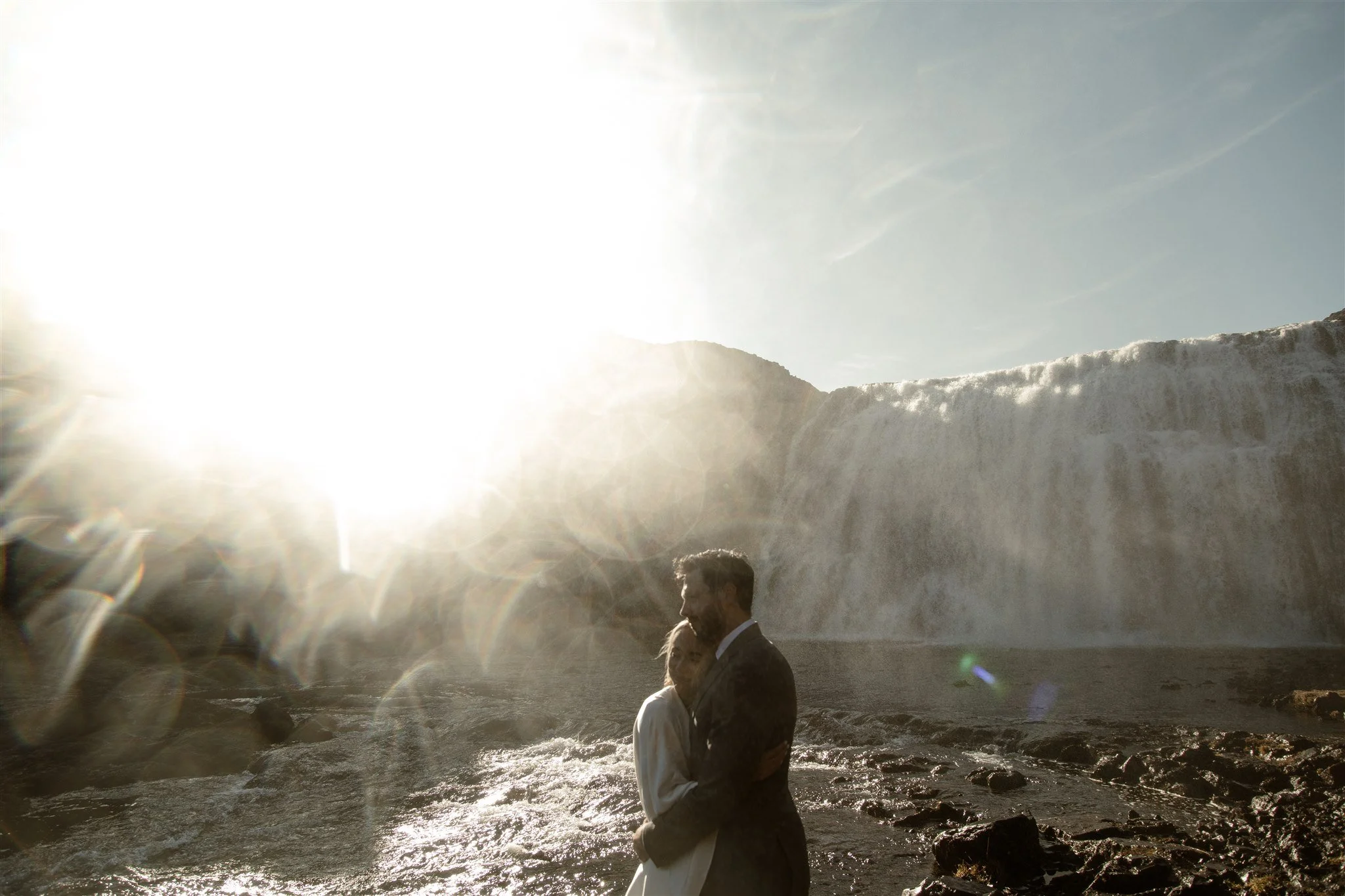 Lord of the Rings Inspired Iceland Engagement Photoshoot at waterfall — couple standing together with Arwen inspired dress with beautiful light and waterfall mist