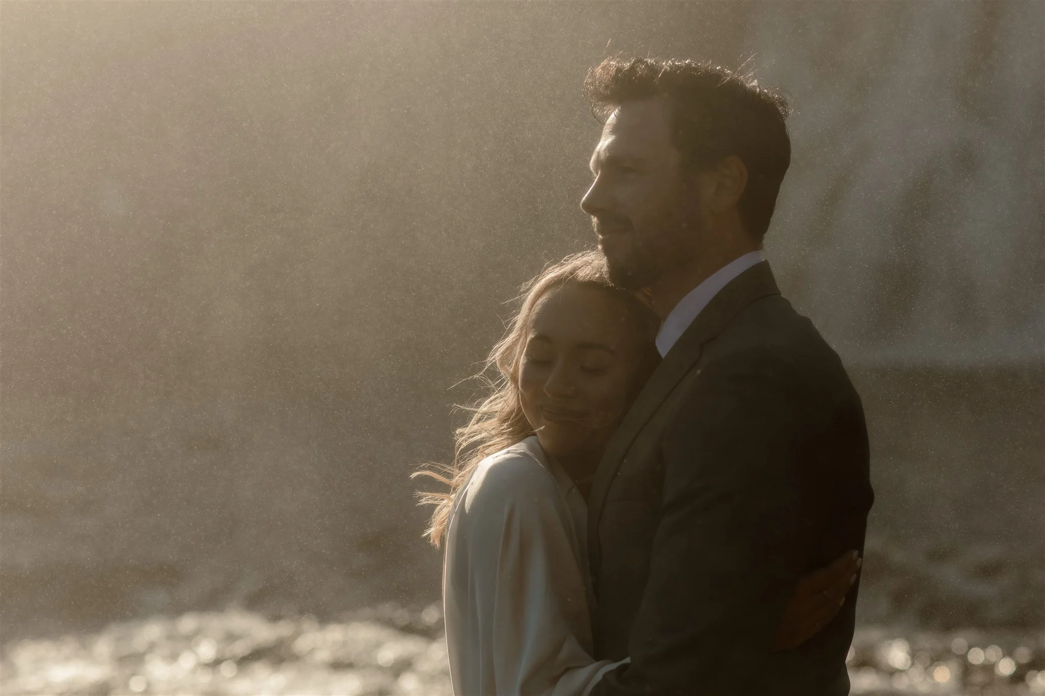 Lord of the Rings Inspired Iceland Engagement Photoshoot at waterfall — couple standing together with Arwen inspired dress with beautiful light and waterfall mist