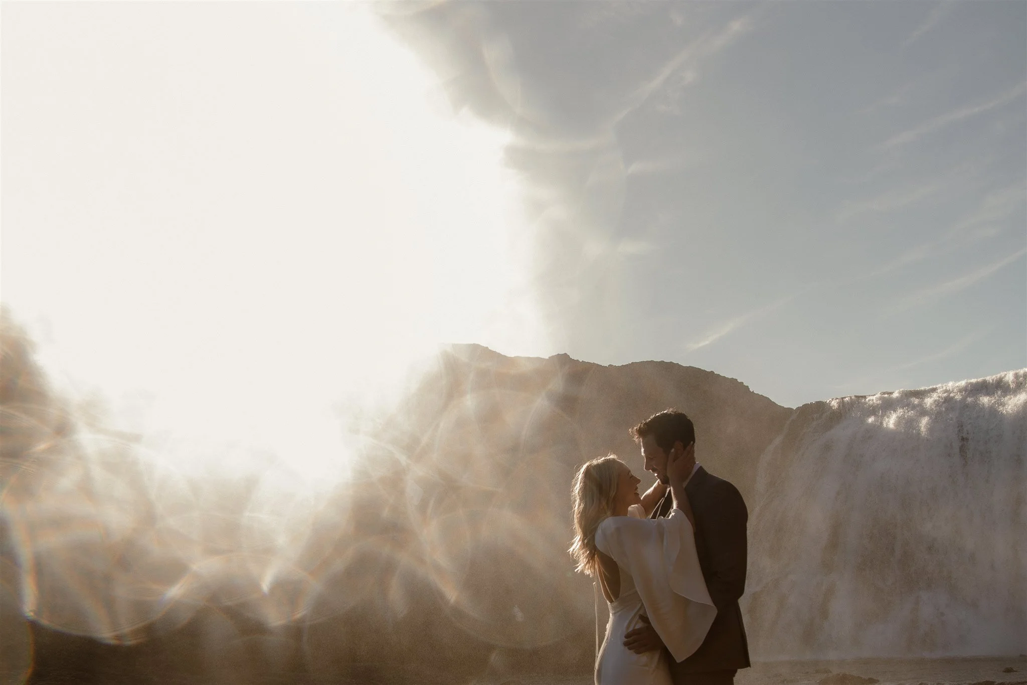 Lord of the Rings Inspired Iceland Engagement Photoshoot at waterfall — couple standing together with Arwen inspired dress with beautiful light and waterfall mist